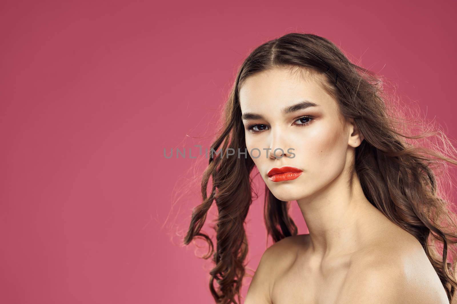 Beautiful brunette woman with makeup on her face on a pink background naked shoulders. High quality photo