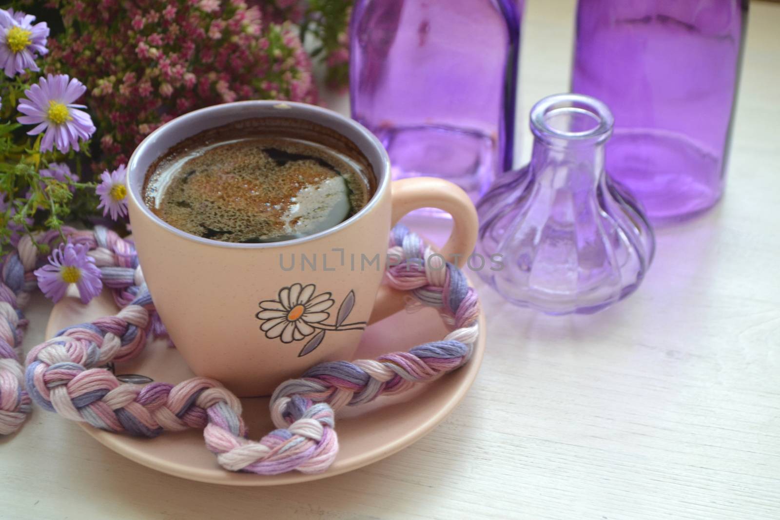 Hot dark coffee in a vintage cup and on an old white wooden background with violet flowers and purple bottles