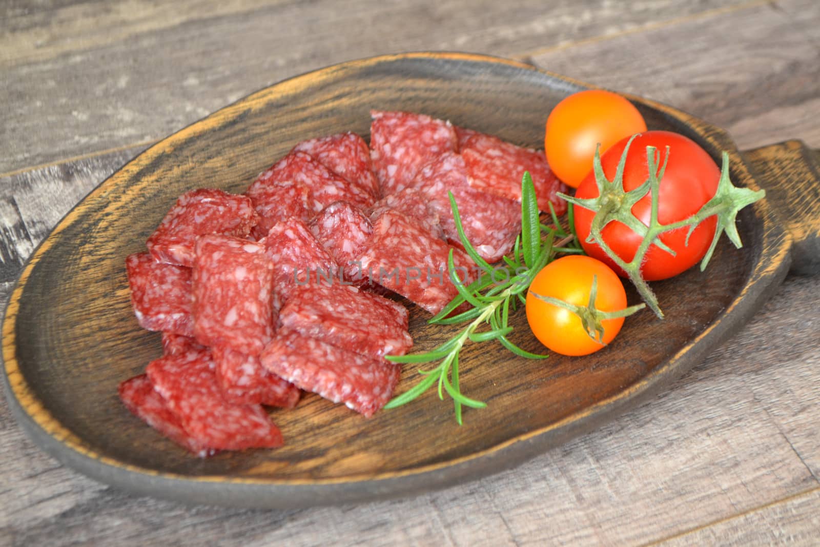 Salami sliced in squares and vegetables on rustic plate.