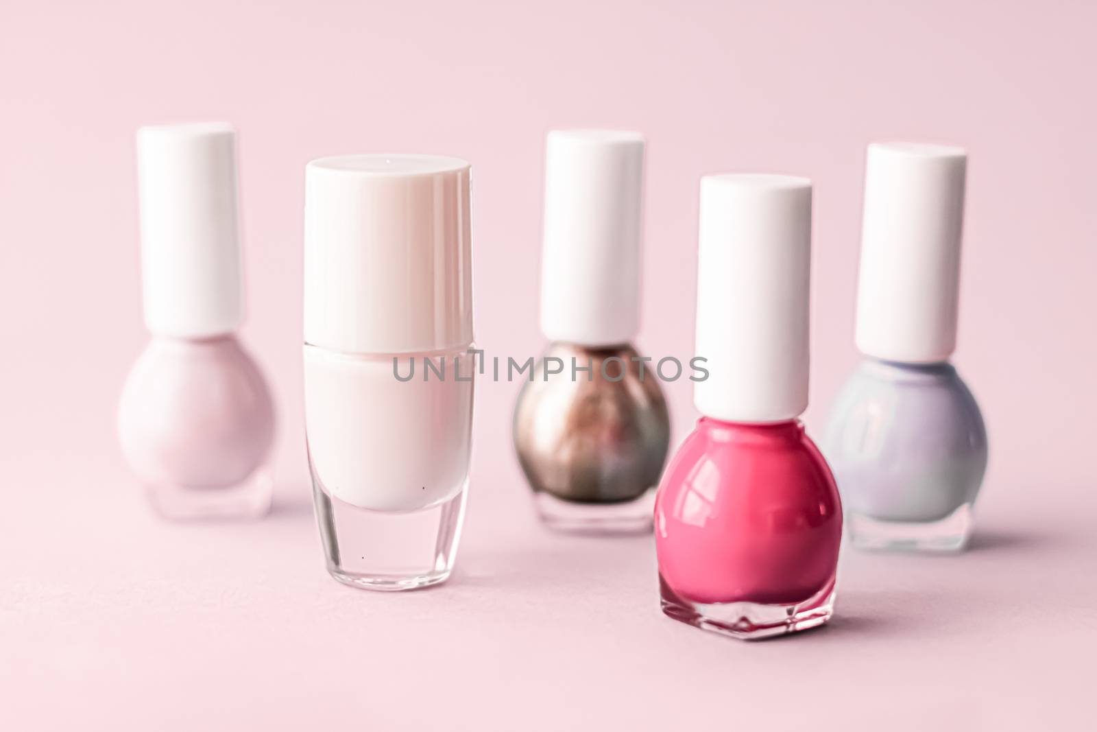 Nail polish bottles on blush pink background, beauty branding