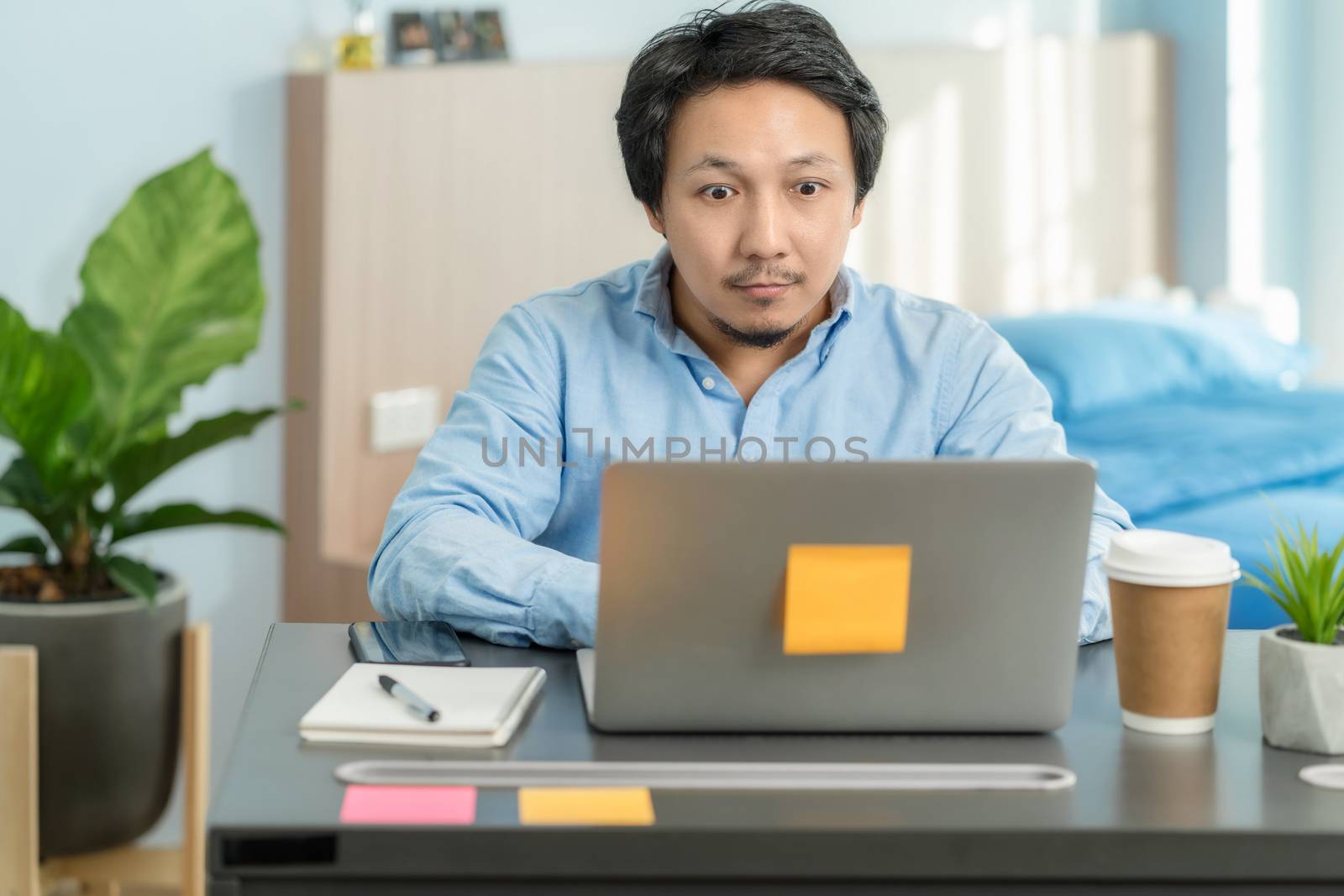 Asian business man using technology laptop and working from home with surprise action in bedroom of house by video conference call,startups and business owner,social distance and new normal concept