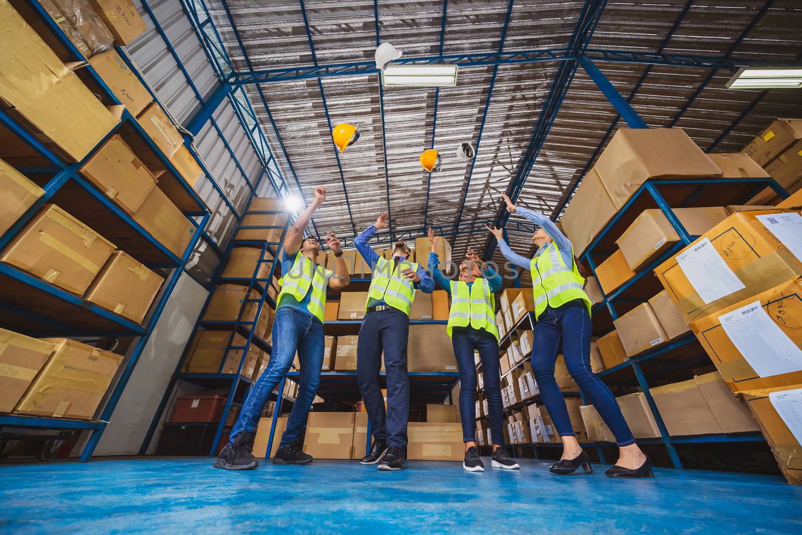 Group of Diversity warehouse worker throwing helmets when success the project and celebrating together in local warehouse, muslim, indian, white caucasian and asian people in export industry concept