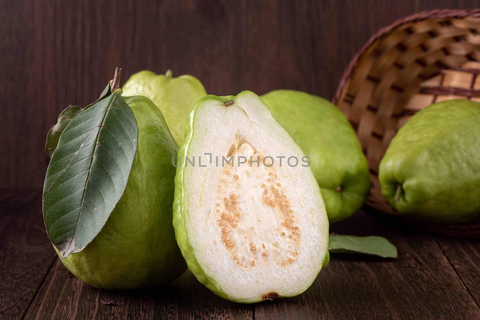 Close up of delicious beautiful guava set with fresh green leaves isolated on dark wooden table background.