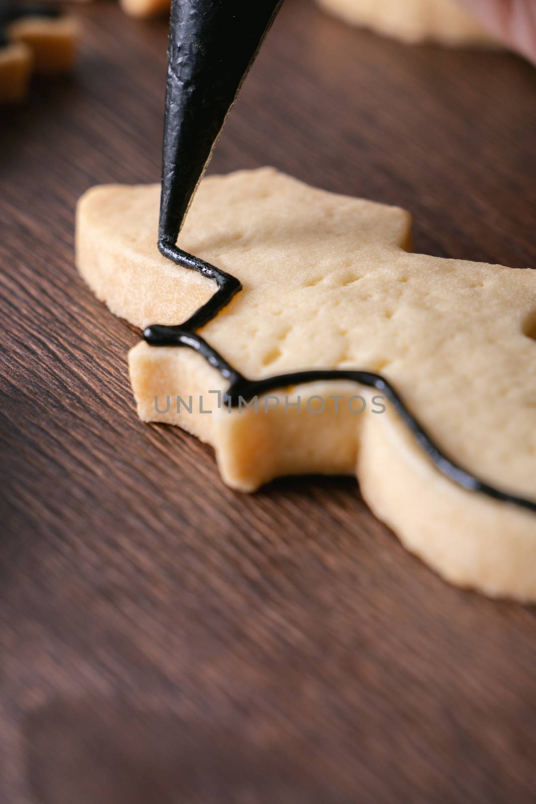 Close up of decorating cute Halloween bat gingerbread sugar cookies with frosting icing cream topping bag.