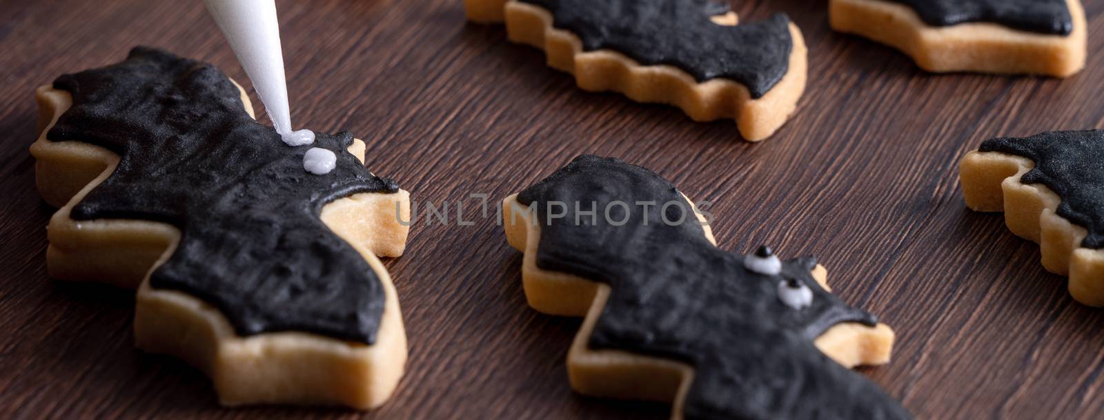 Close up of decorating cute Halloween bat gingerbread sugar cookies with frosting icing cream topping bag.