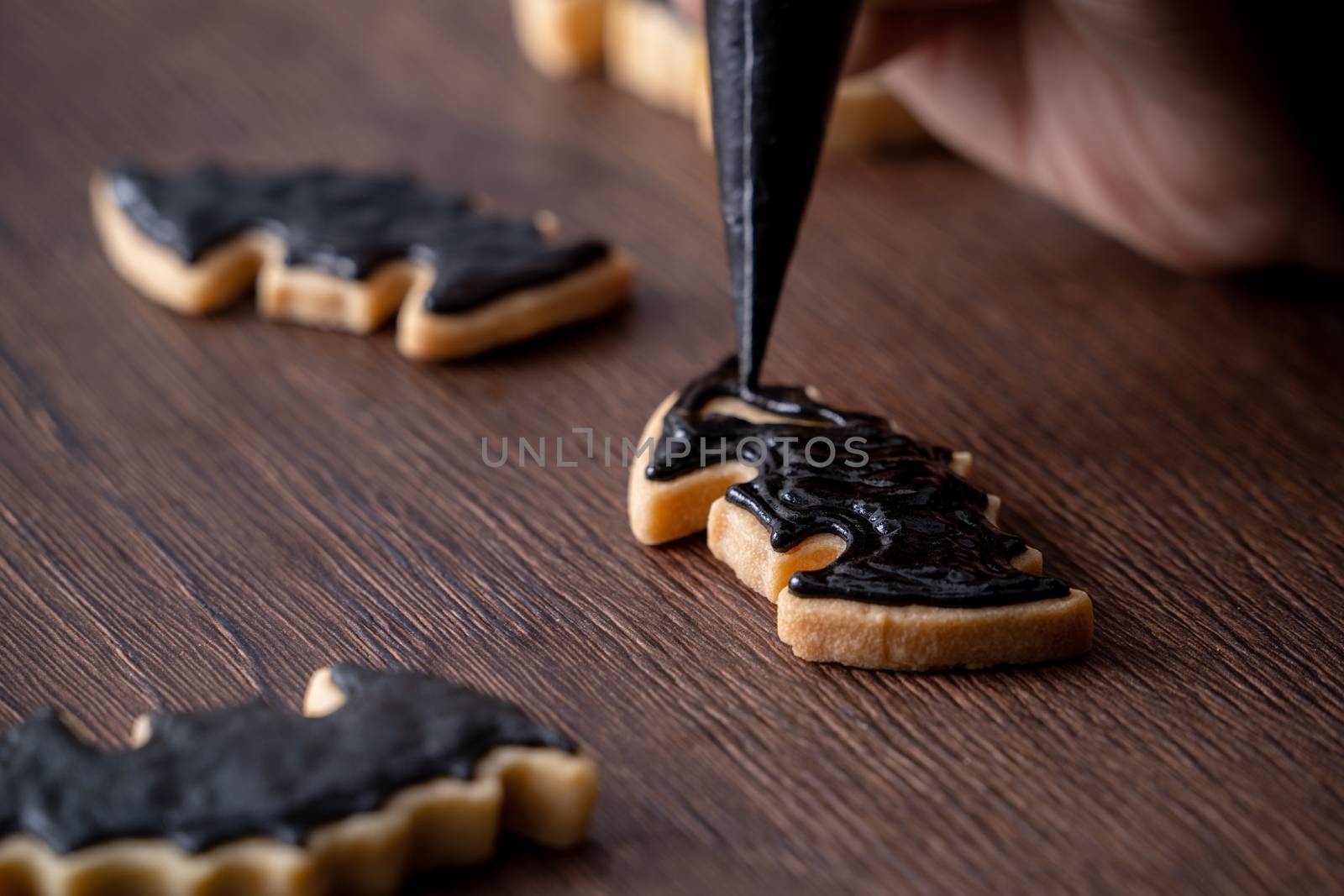 Close up of decorating cute Halloween bat gingerbread sugar cookies with frosting icing cream topping bag.