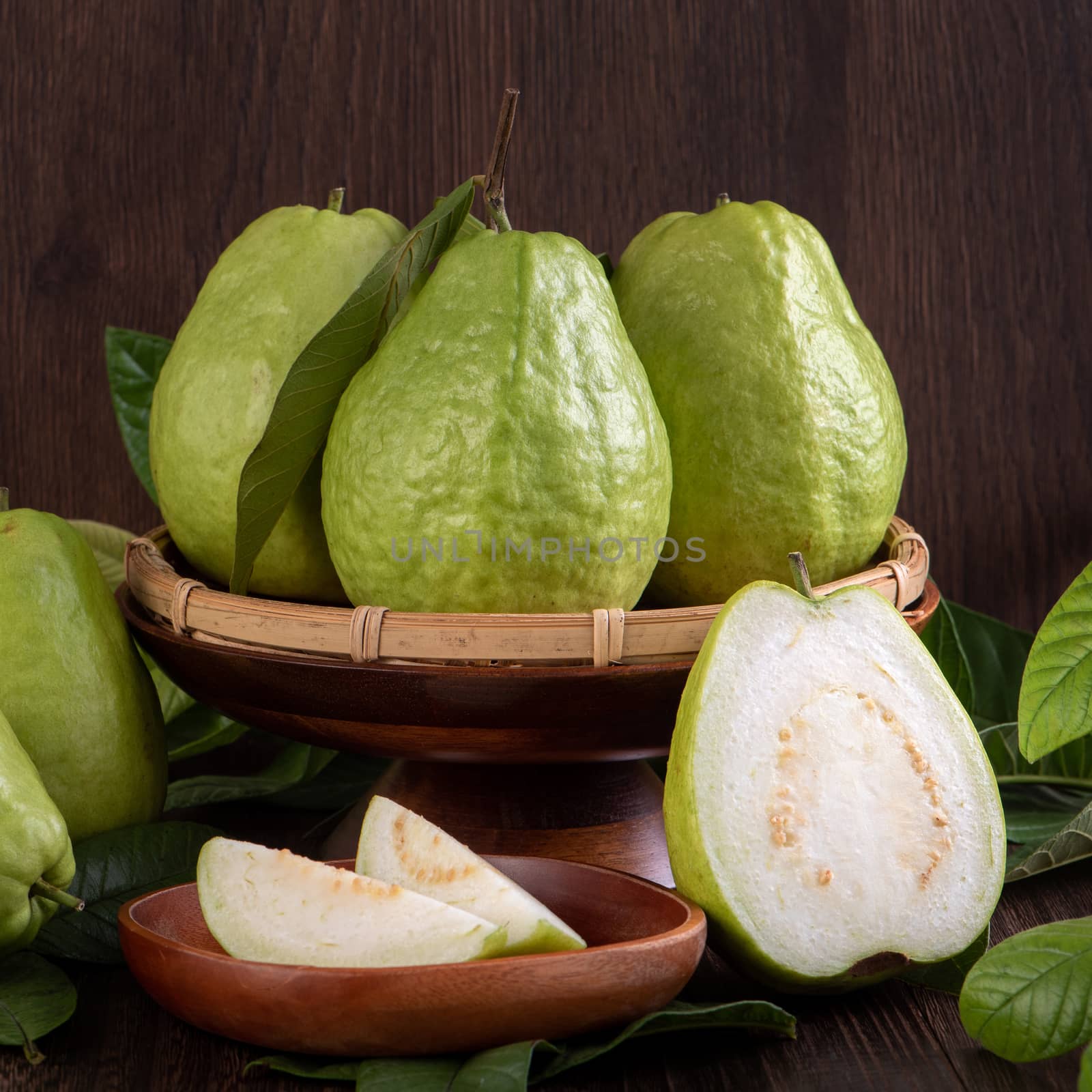 Close up of delicious beautiful guava set with fresh green leaves isolated on dark wooden table background.