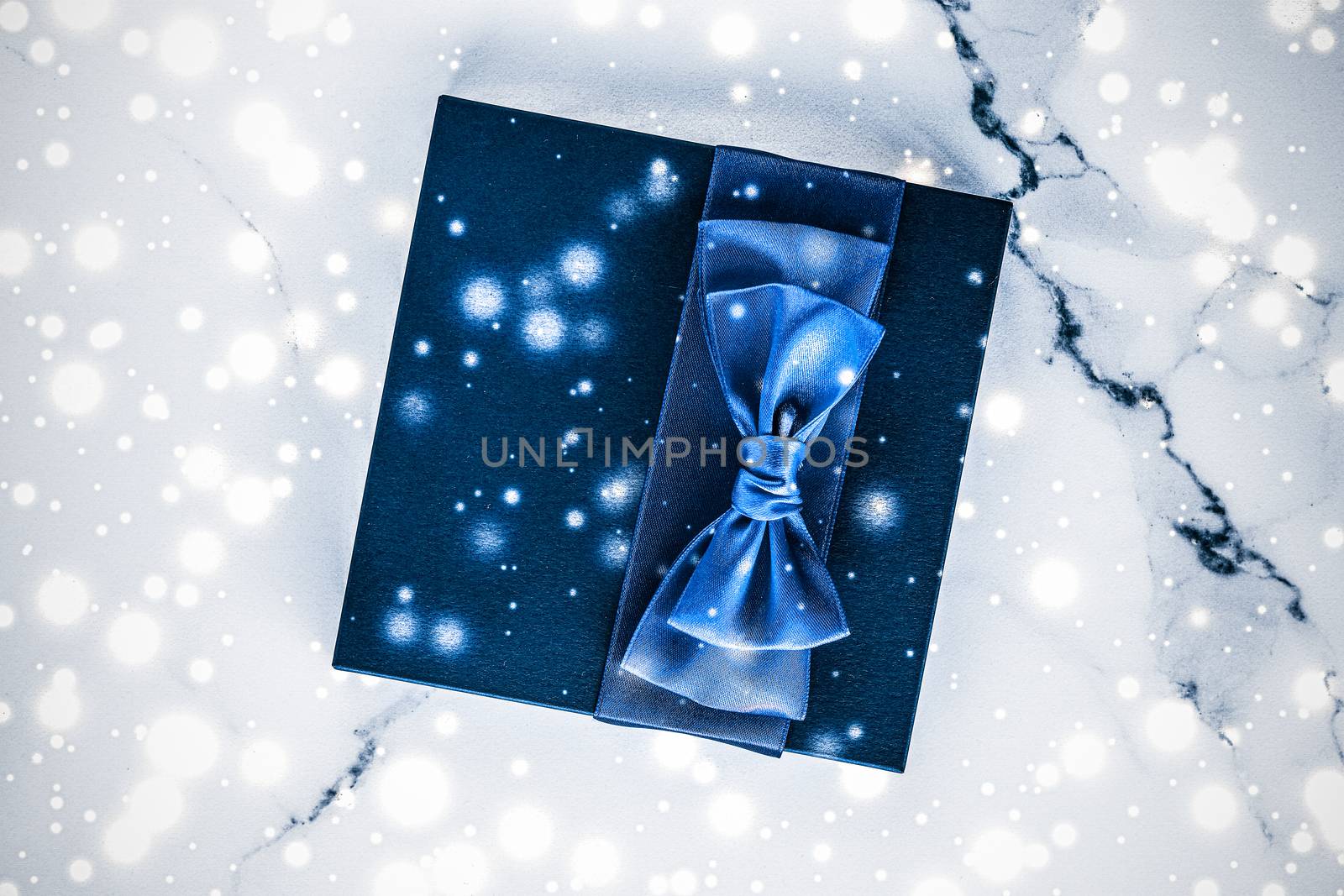 Branding, glamour and cold season concept - Winter holiday gift box with blue silk bow, snow glitter on marble background as Christmas and New Years presents for luxury beauty brand, flatlay design