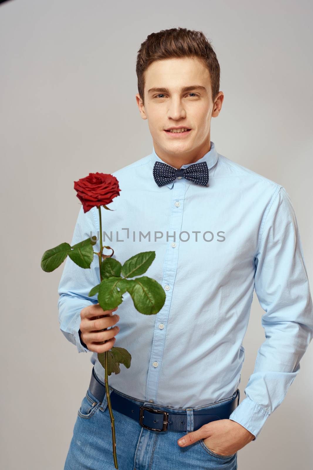 Romantic man with a red rose and in a blue shirt with a bow tie around his neck gray background. High quality photo