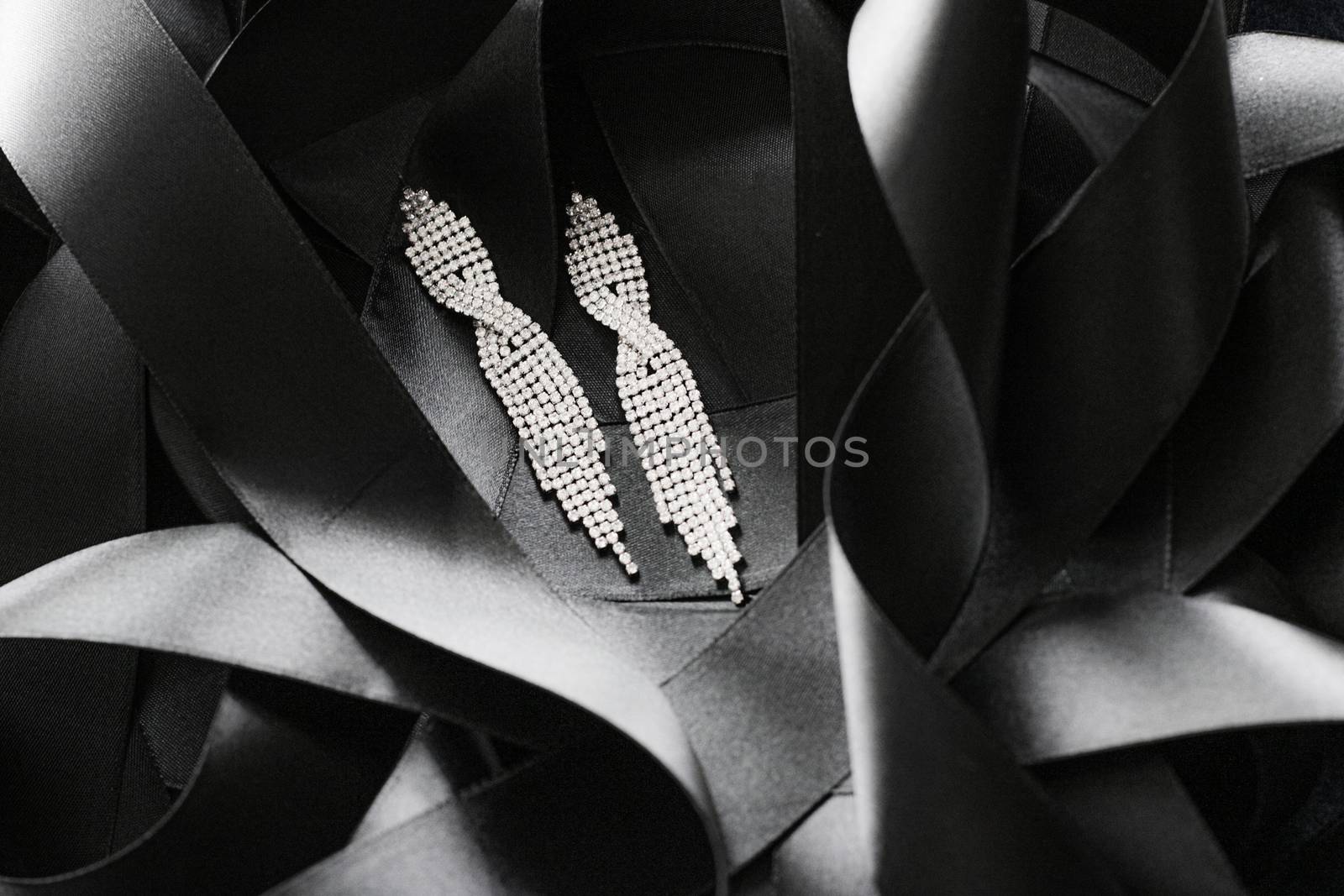 Luxury diamond earrings on black silk ribbon as background, jewelry and fashion brands