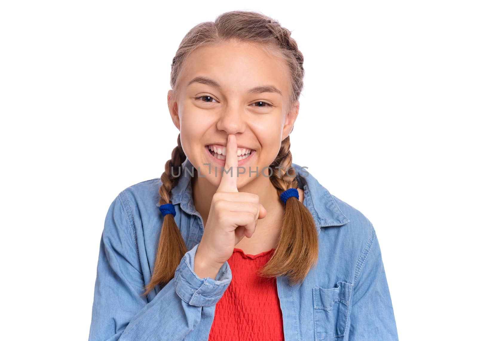 Happy teenage girl keeps fore finger on lips, asking for silence, isolated on white background