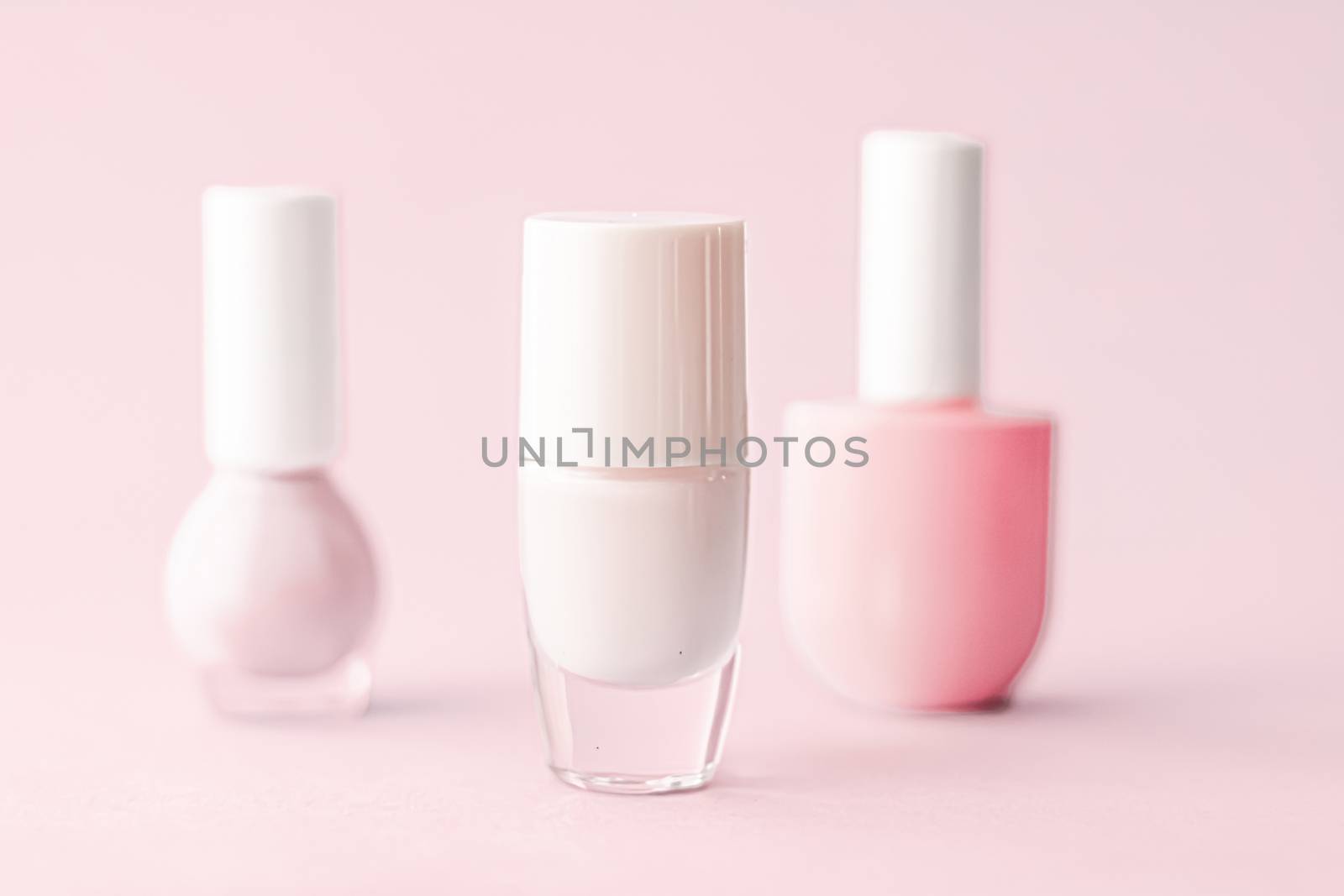 Nail polish bottles on blush pink background, beauty branding