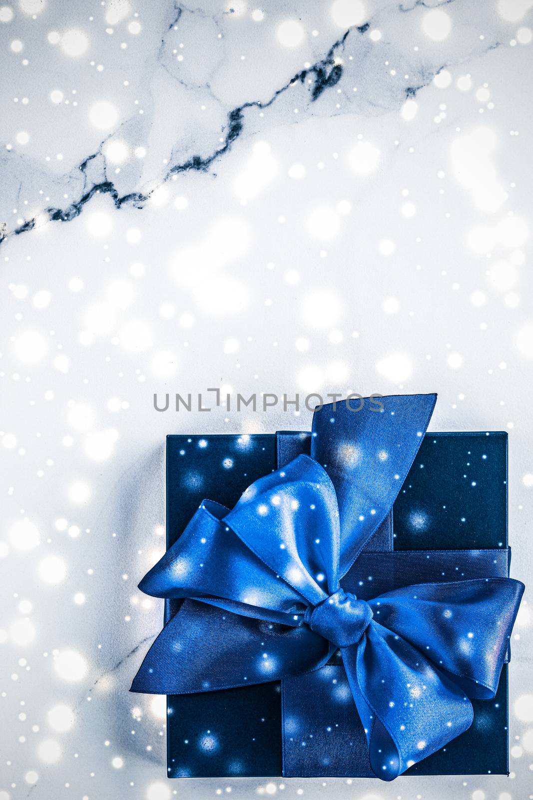 Branding, glamour and cold season concept - Winter holiday gift box with blue silk bow, snow glitter on marble background as Christmas and New Years presents for luxury beauty brand, flatlay design