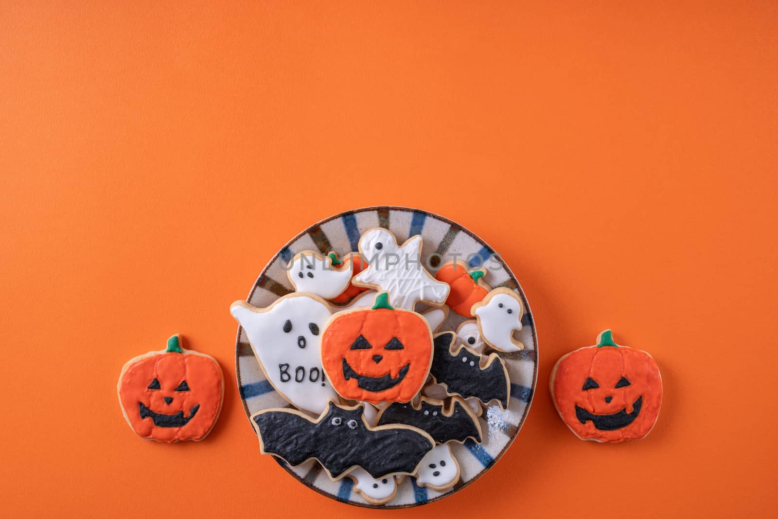 Top view of Halloween festive decorated icing gingerbread sugar cookies on orange background with copy space and flat lay layout.