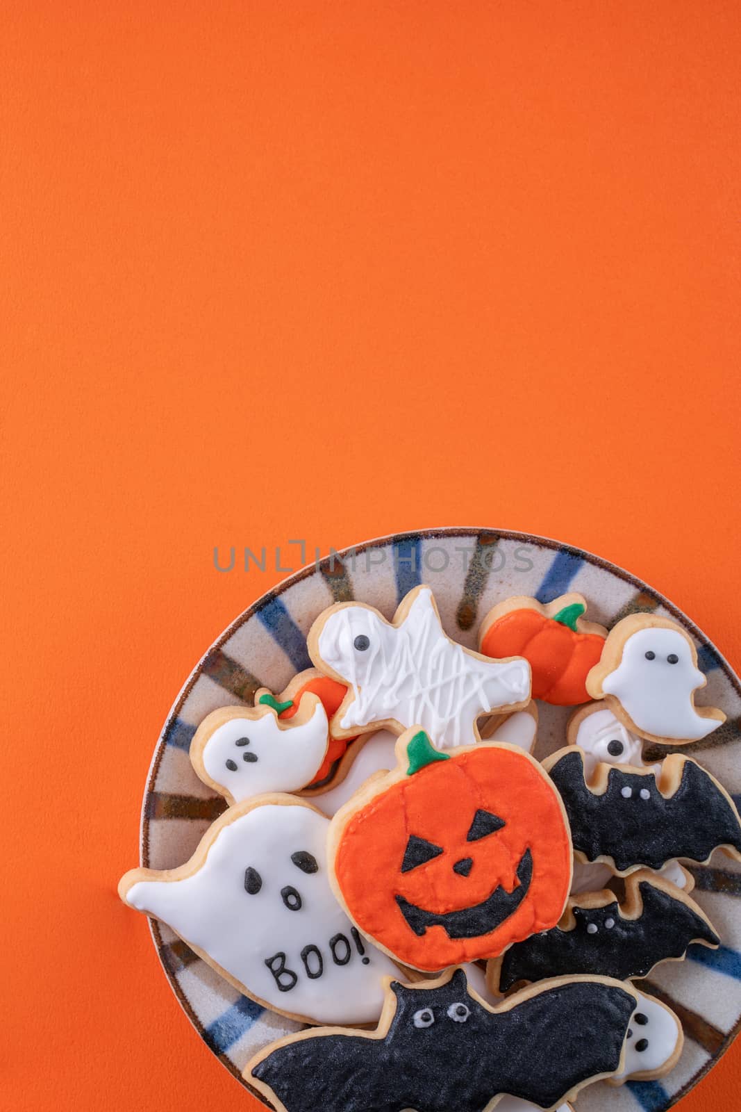 Top view of Halloween festive decorated icing gingerbread sugar cookies on orange background with copy space and flat lay layout.