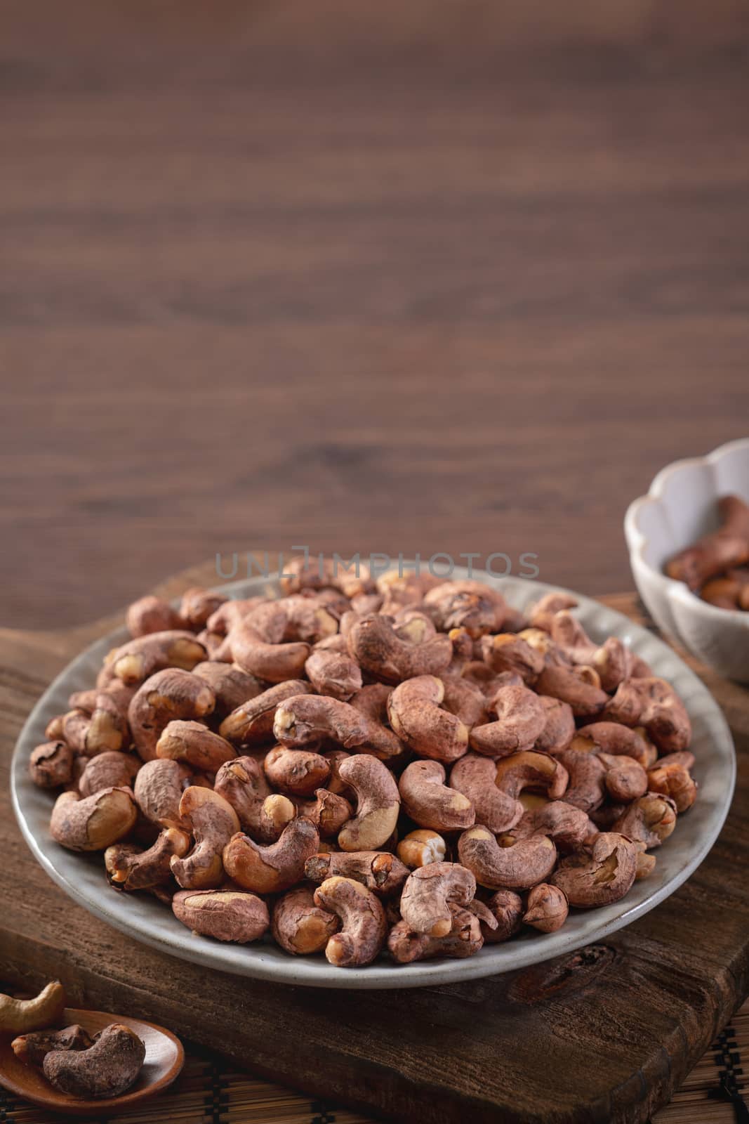 Cashew nuts with peel in a plate on wooden tray and table background, healthy raw food concept.