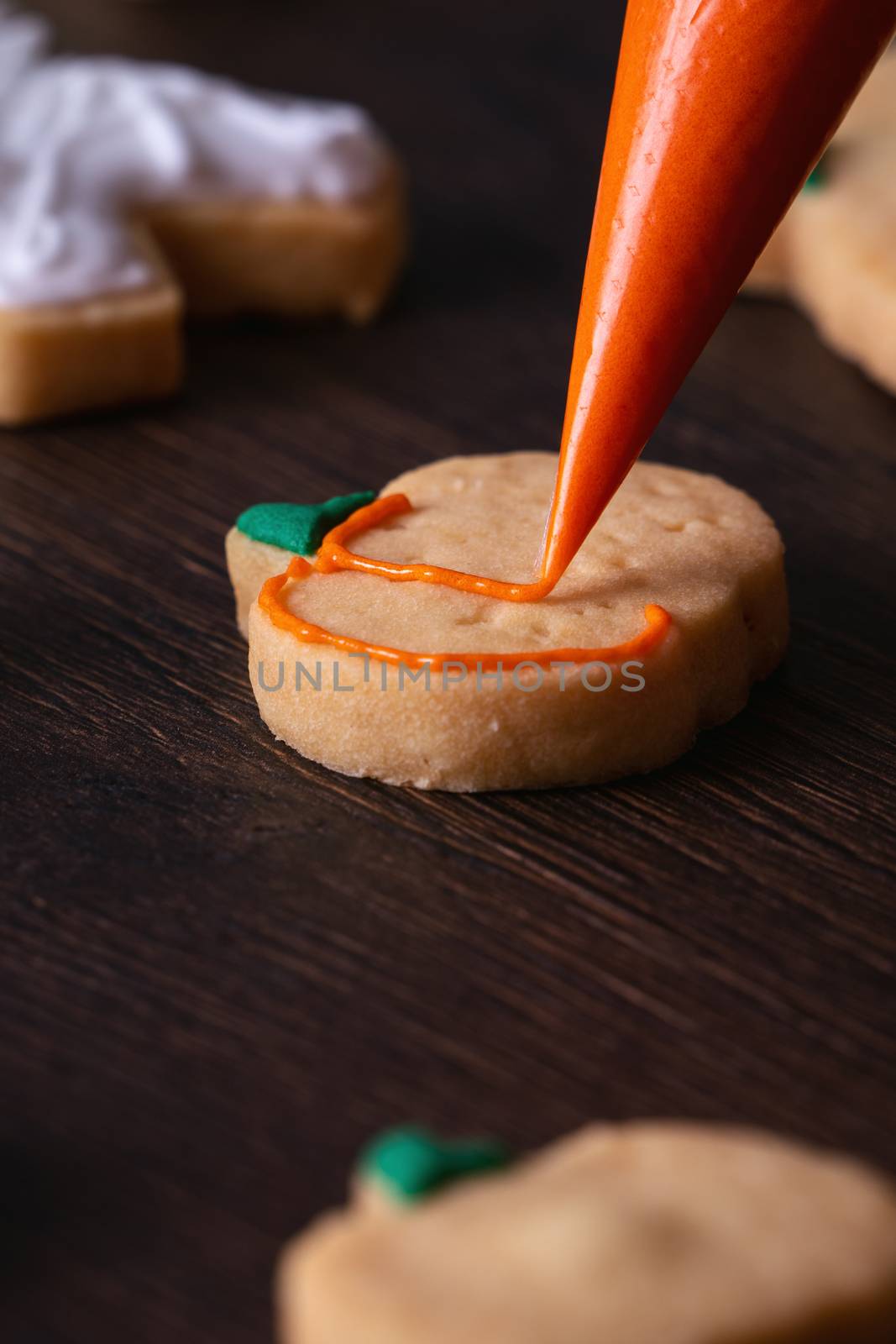 Close up of decorating cute Halloween pumpkin gingerbread cookies with frosting icing cream topping bag.