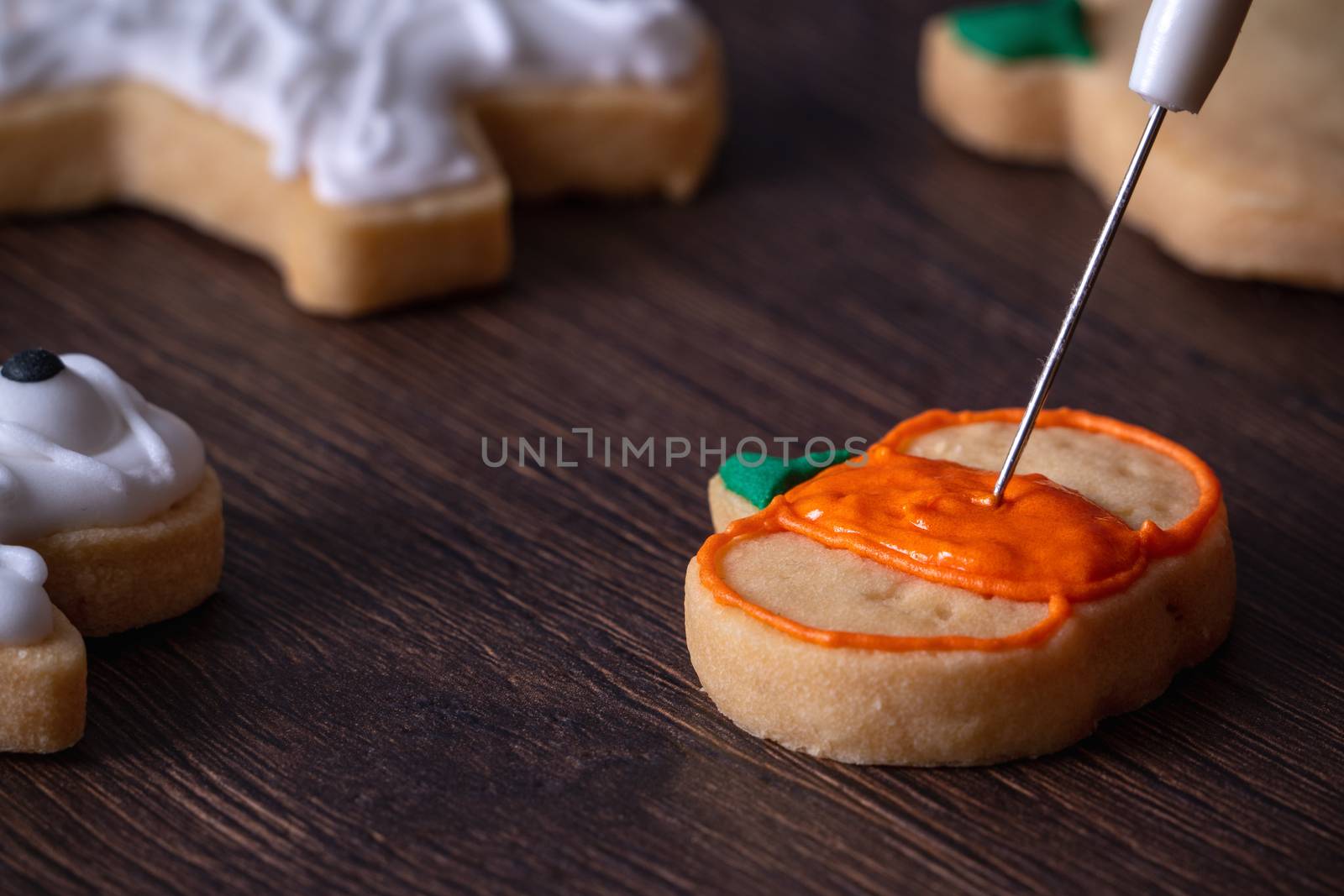 Close up of decorating cute Halloween pumpkin gingerbread cookies with frosting icing cream topping bag.