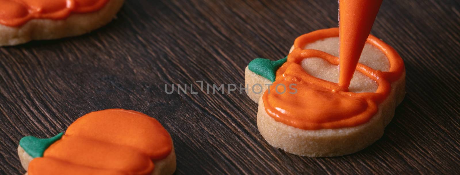 Close up of decorating cute Halloween pumpkin gingerbread cookies with frosting icing cream topping bag.