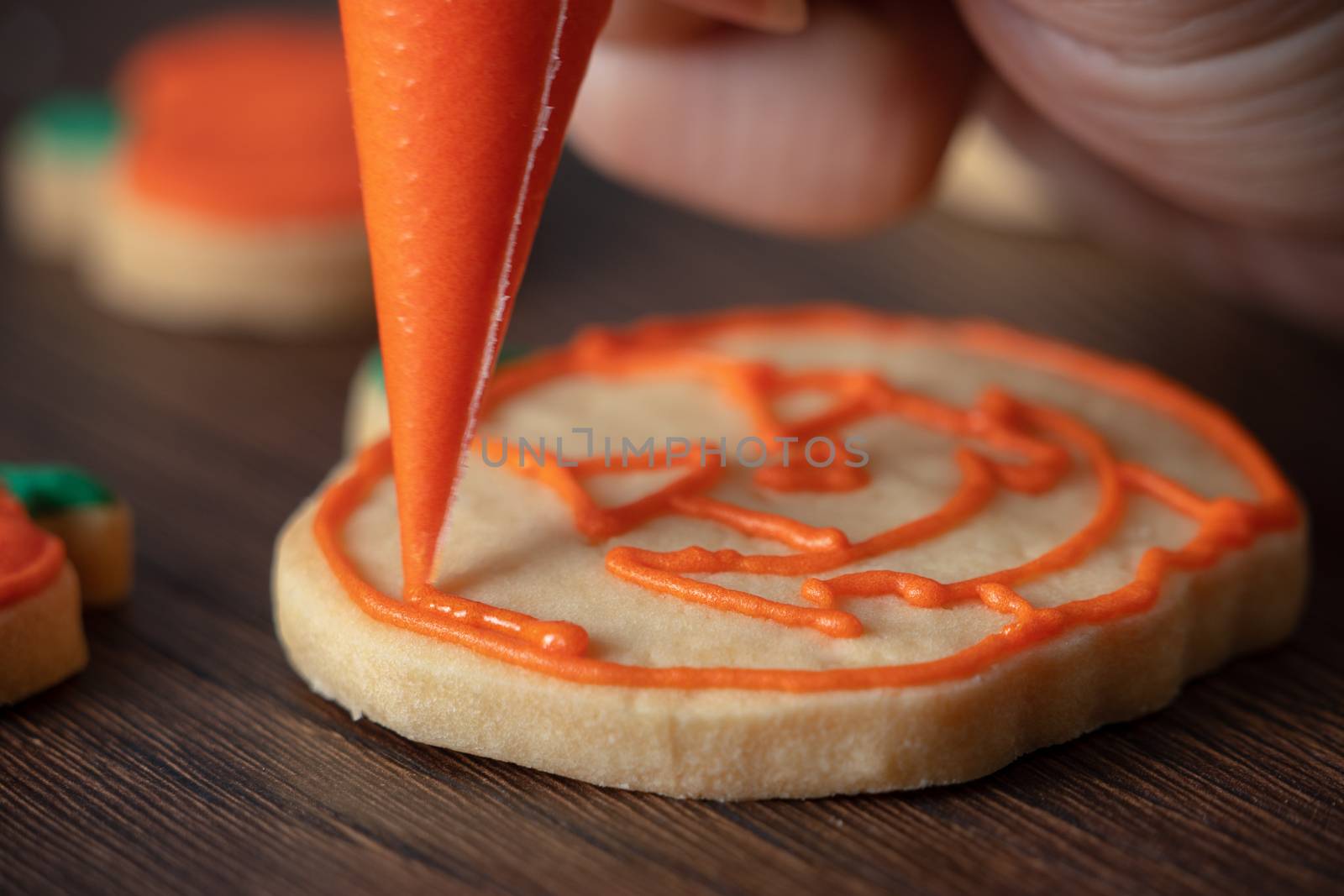 Close up of decorating cute Halloween pumpkin gingerbread cookies with frosting icing cream topping bag.