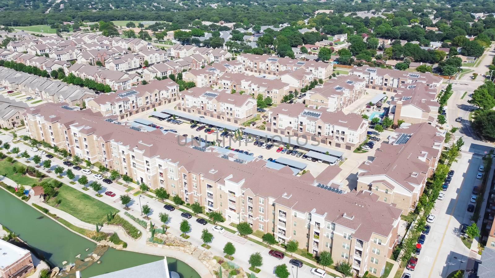 Brand new multistory apartment complex with covered parking lots and suburban residential area in background. Master-planned community and census-designated sprawl in Flower Mound, TX