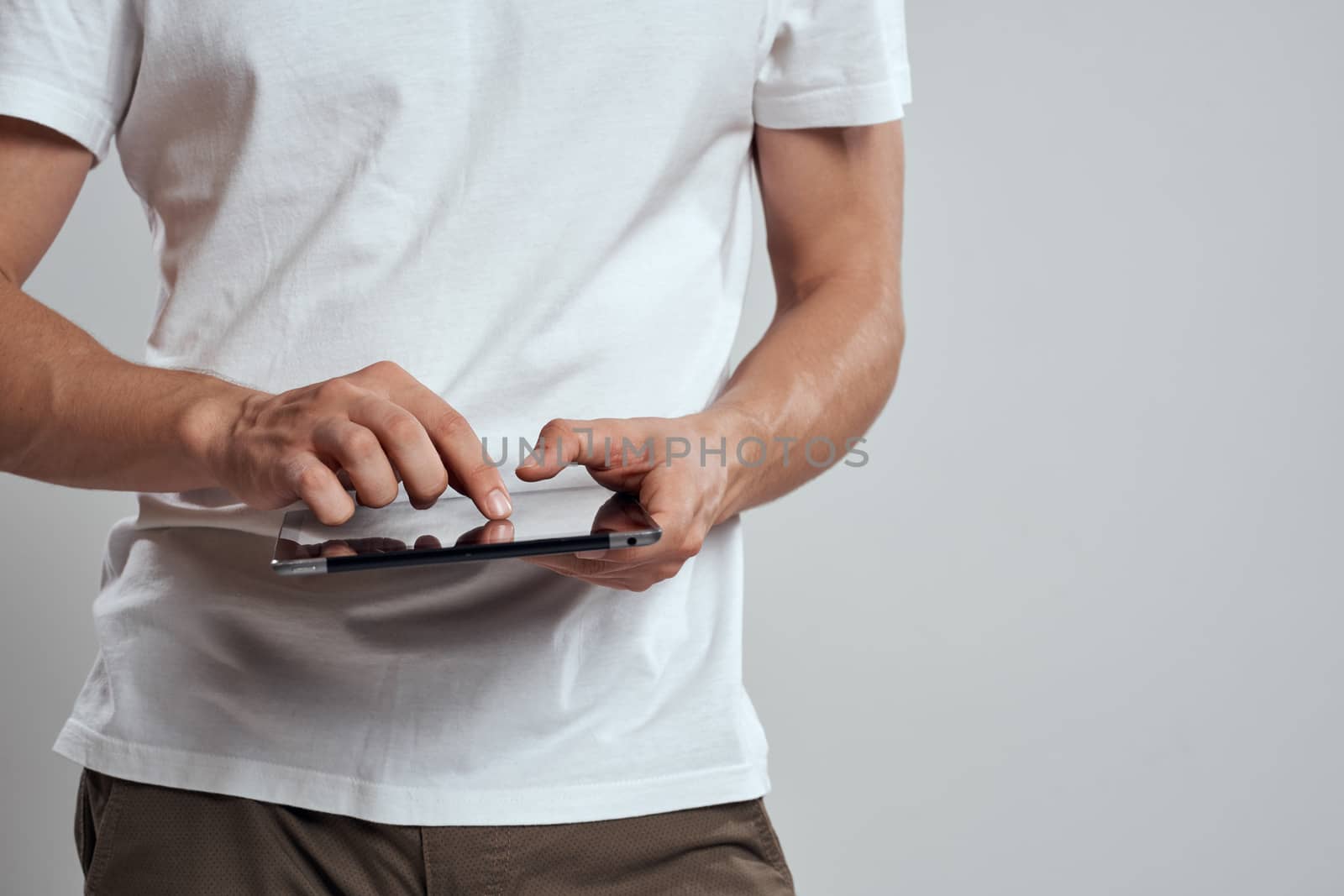 Tablet with a touch screen on a light background male hands white t-shirt cropped view by SHOTPRIME