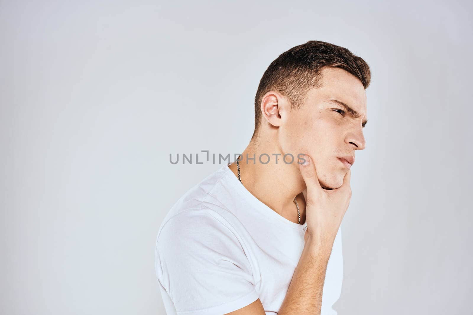 Emotional man in a white t-shirt holds his hand on his face light background. High quality photo