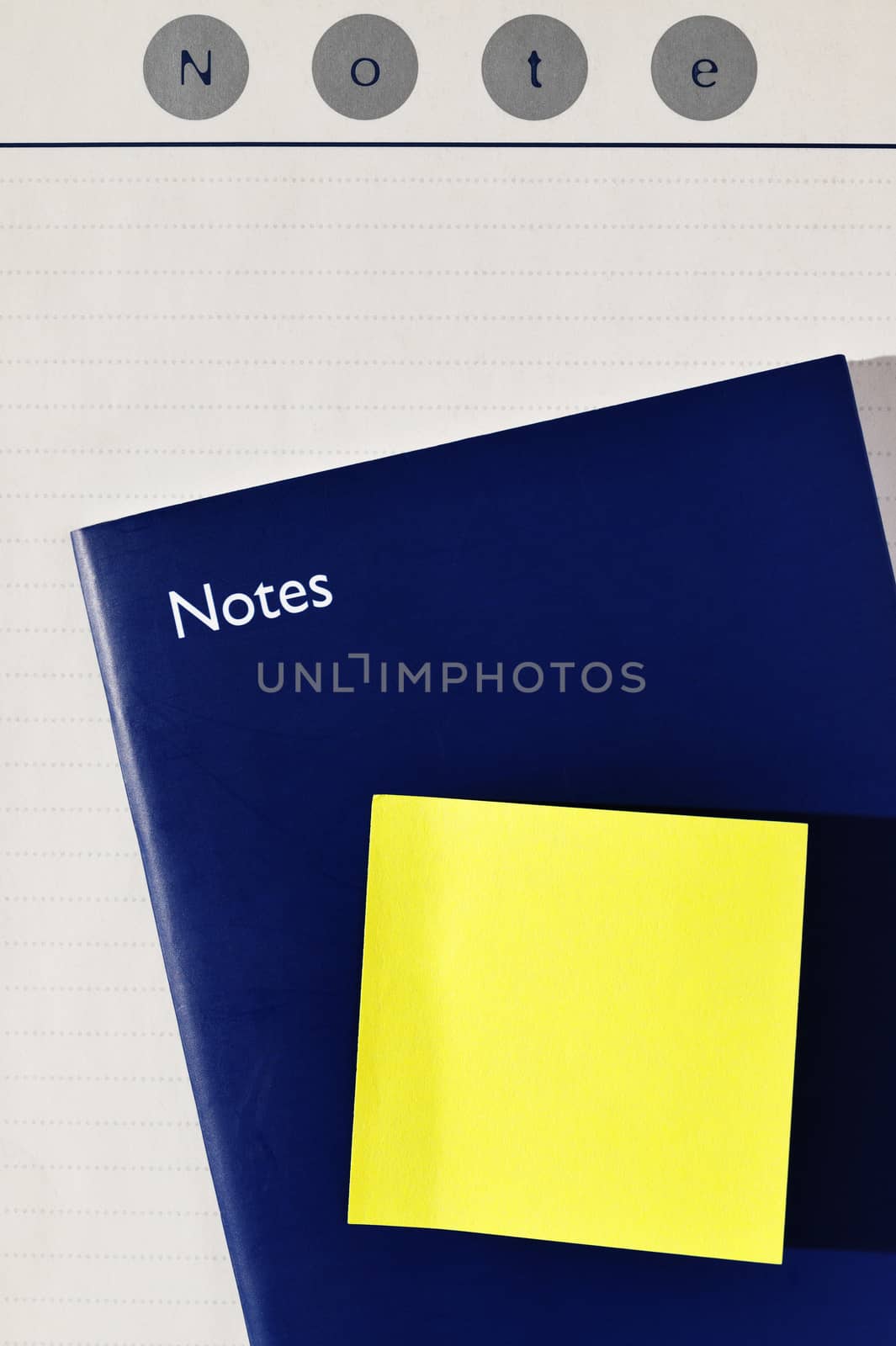 Yellow post-it note , closed blue notebook and white agenda page with word NOTE