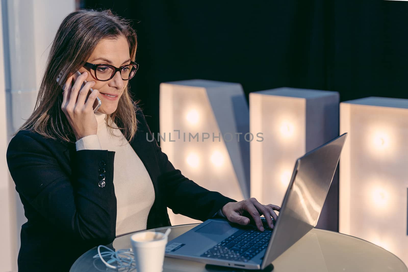 Adult gorgeous woman having smart phone conversation while sitting in front of open laptop computer in cafe bar, attractive female calling with her cell telephone while she breakfast in coffee shop