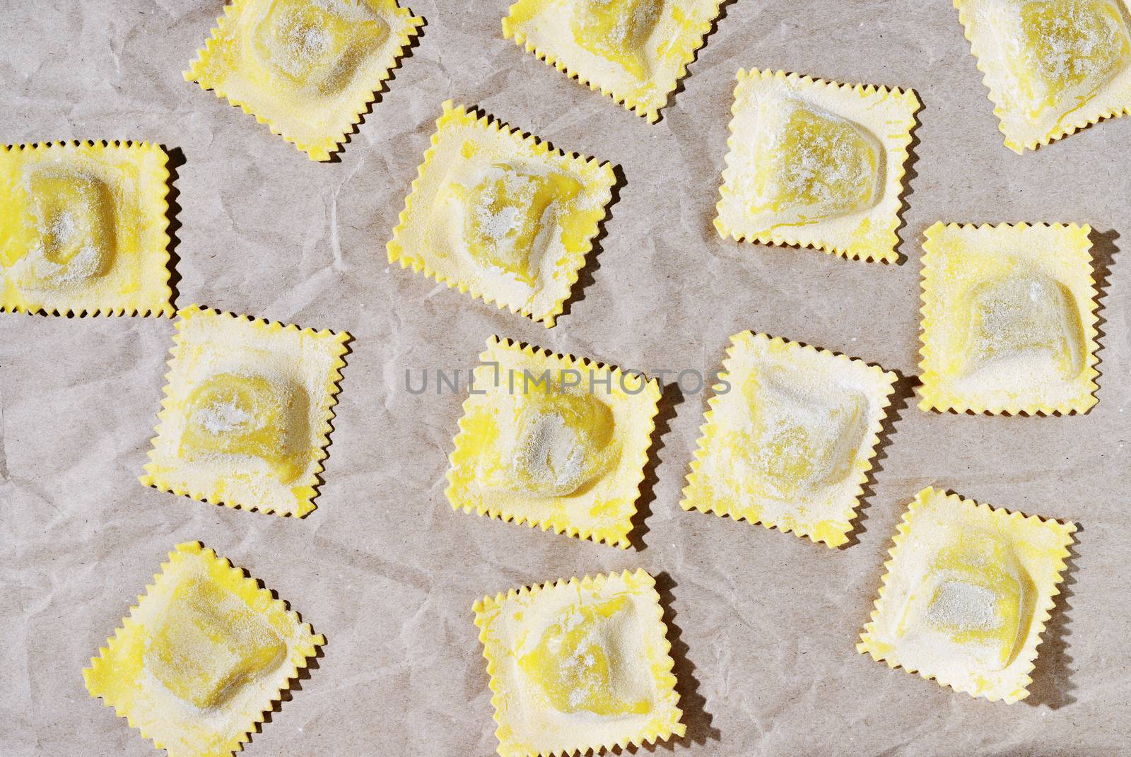 Square uncooked ravioli with flour on brown paper .