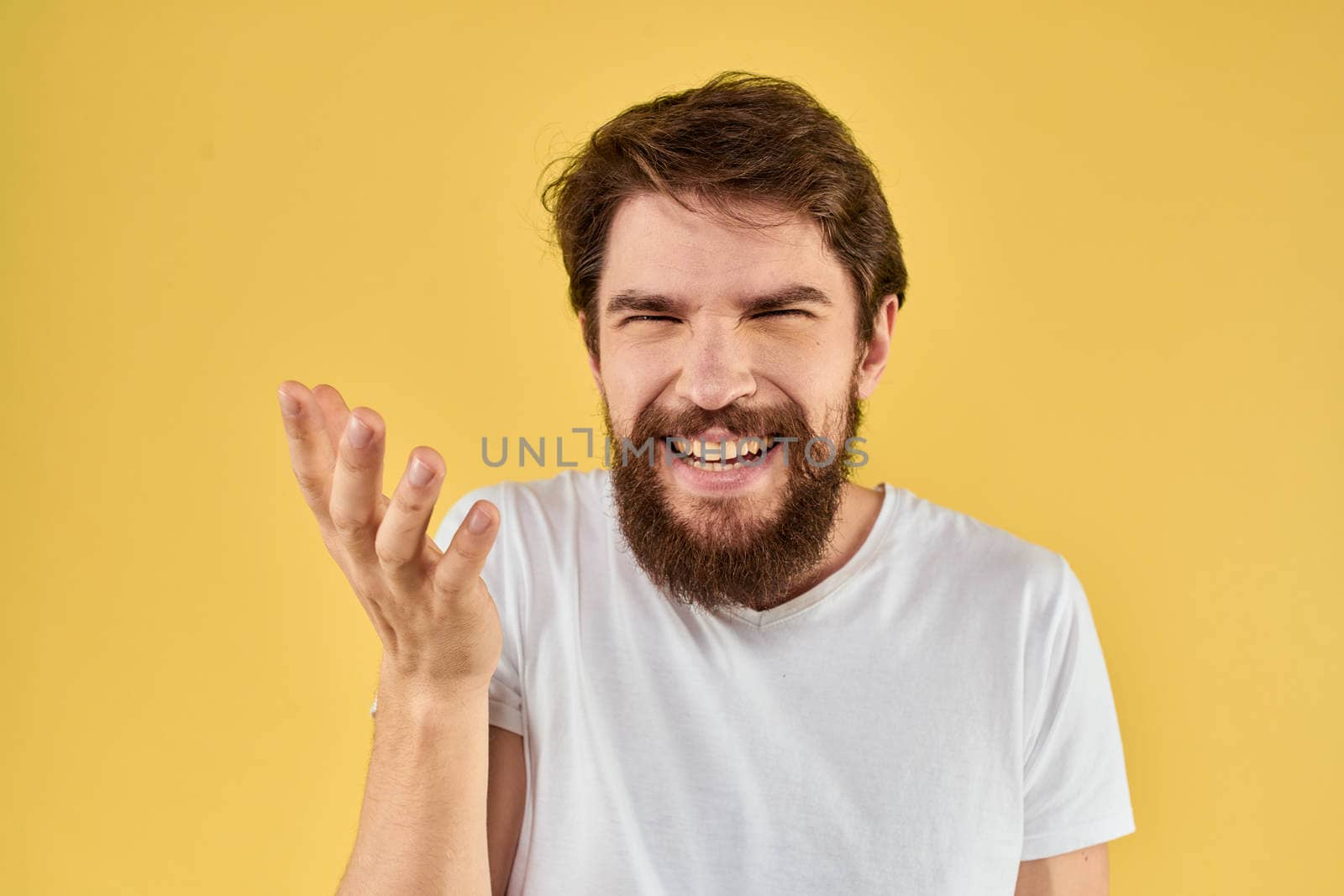 Bearded man emotions fun gesture with hands white t-shirt close-up yellow background. High quality photo