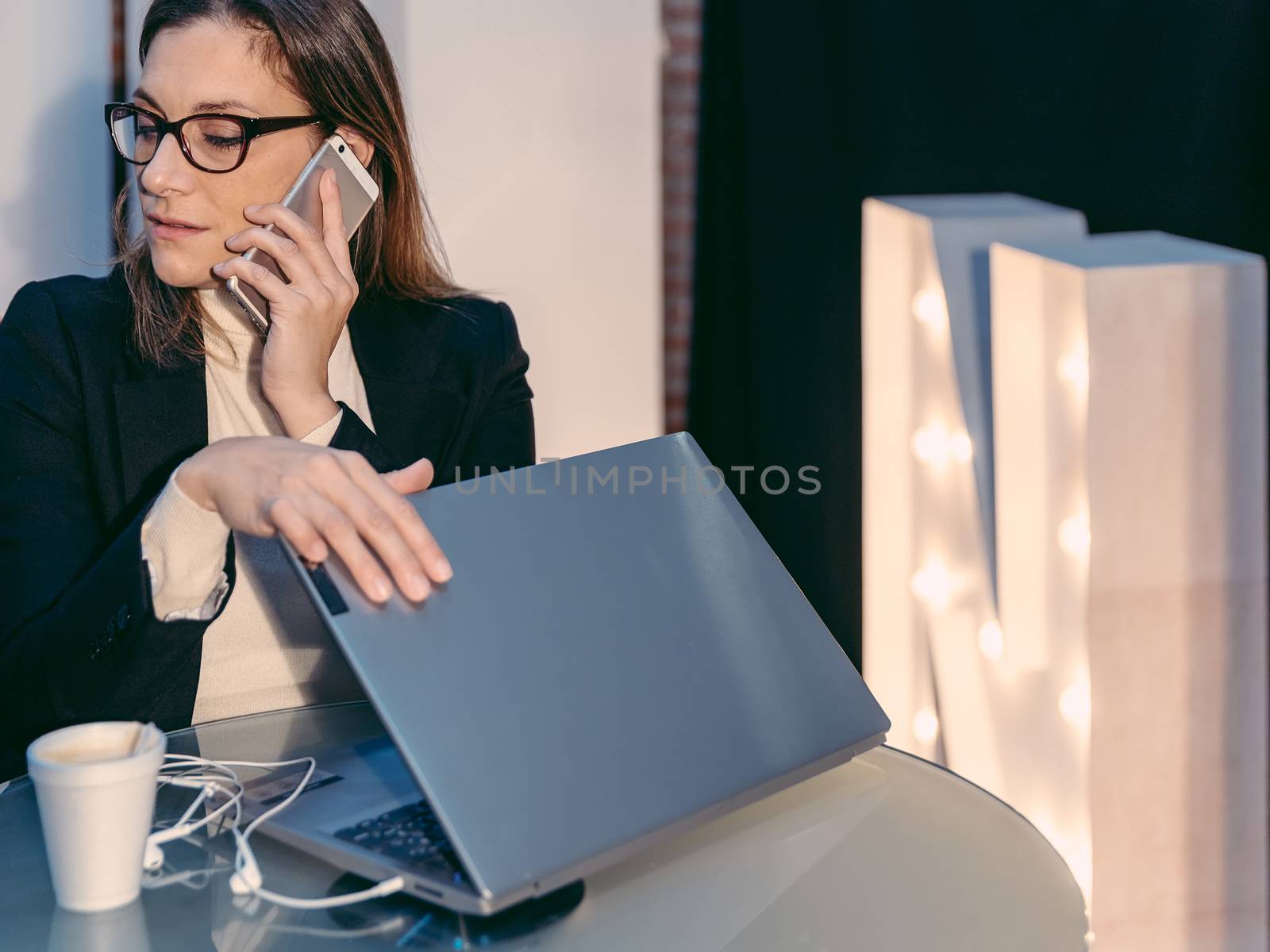 woman having phone conversation while closing laptop computer in cafe bar by JRPazos