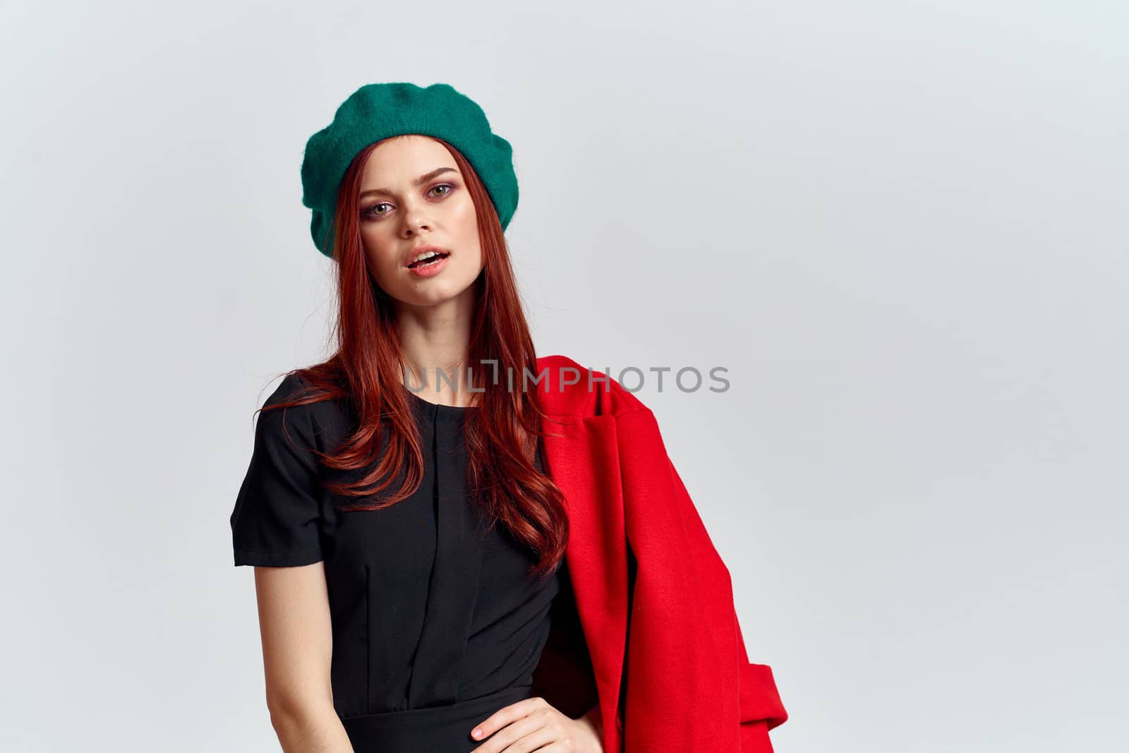 A woman holds in her hand a red coat and a dark T-shirt Green hat cropped view of a light background by SHOTPRIME