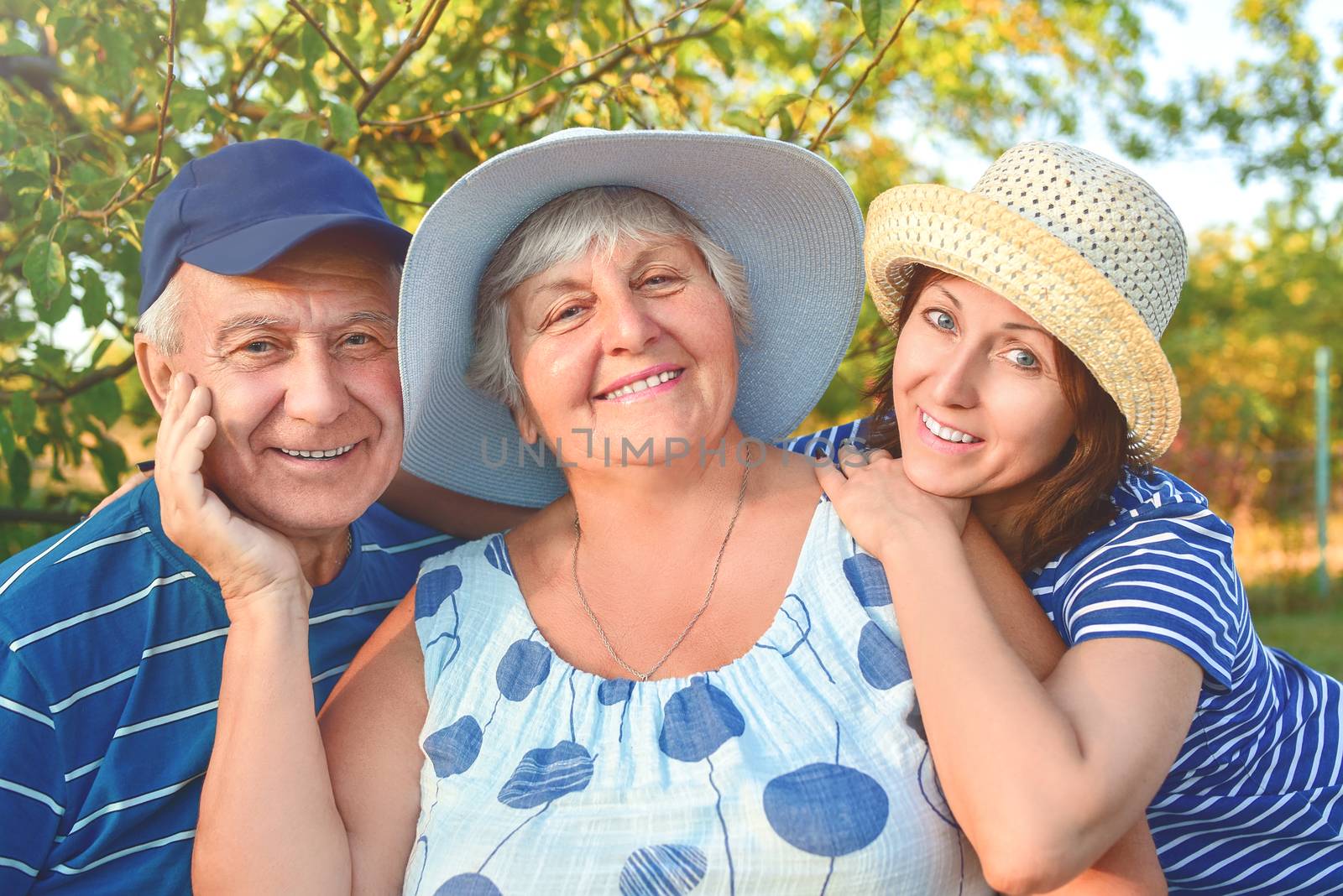 Beautiful old couple is sitting on the bench in the park with their adult daughter. Grandma and grandpa are hugging and smiling. Real love and family relationship photo. Generations concept. by Nickstock