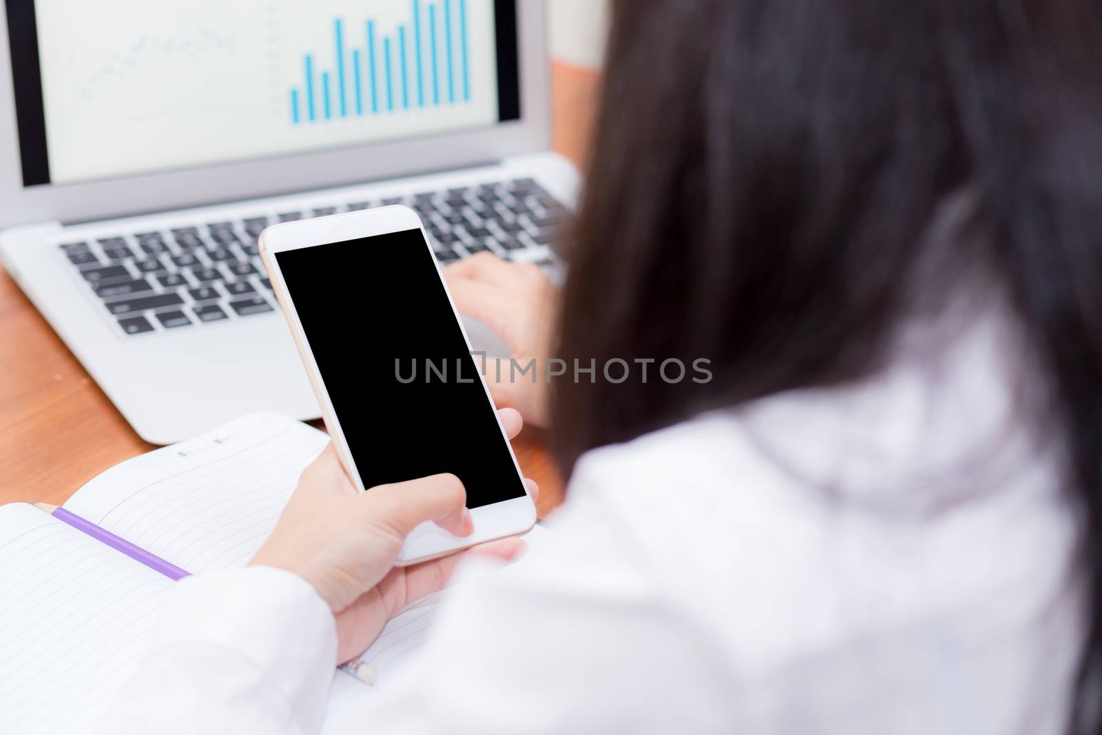 Asian woman hand holding a white phone with screen above on desk, girl using mobile with laptop, communication online digital concept.