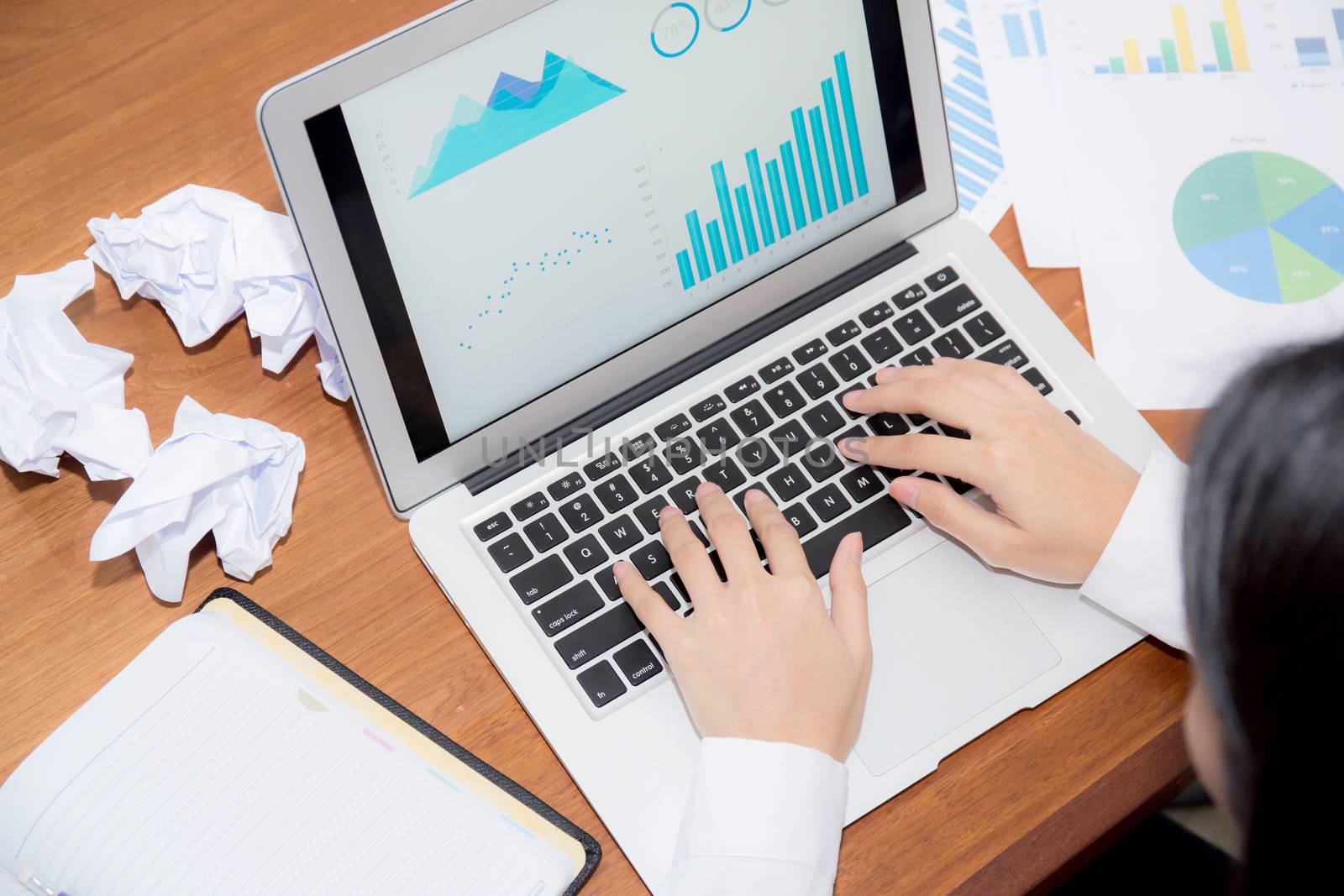 Businesswoman tired and stressed with overworked at desk, girl with worried not idea with graph analysis laptop and crumpled paper at office, business concept.