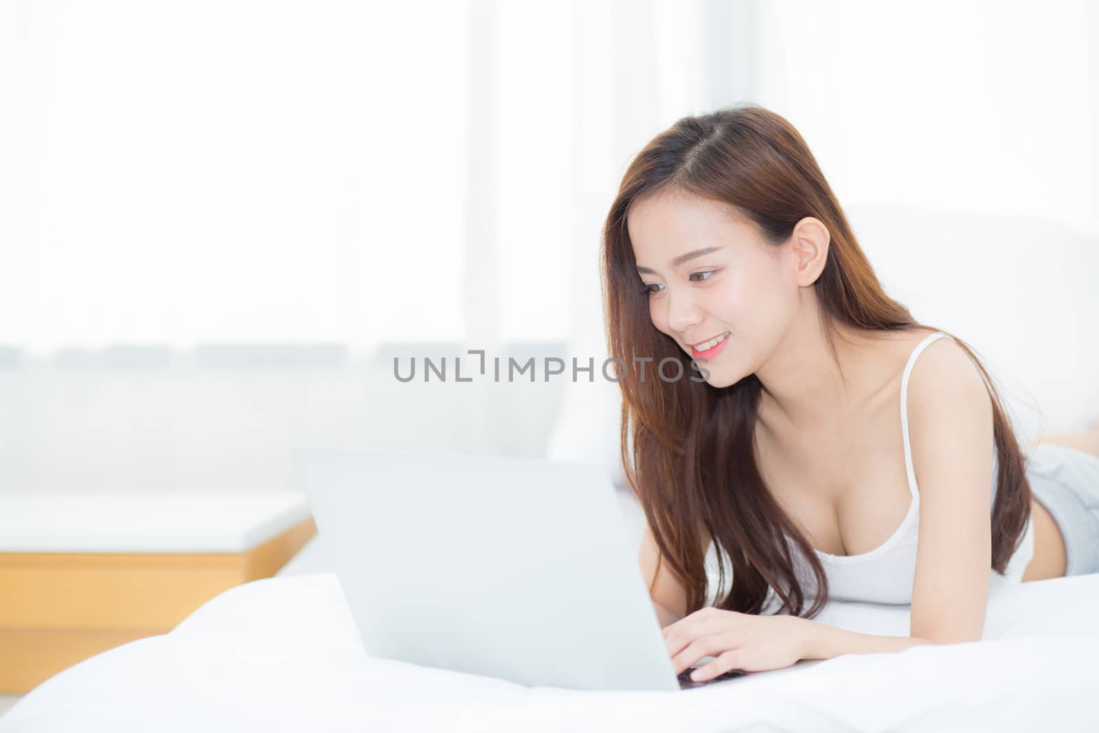 Beautiful asian young woman lying on bed using laptop at bedroom by nnudoo