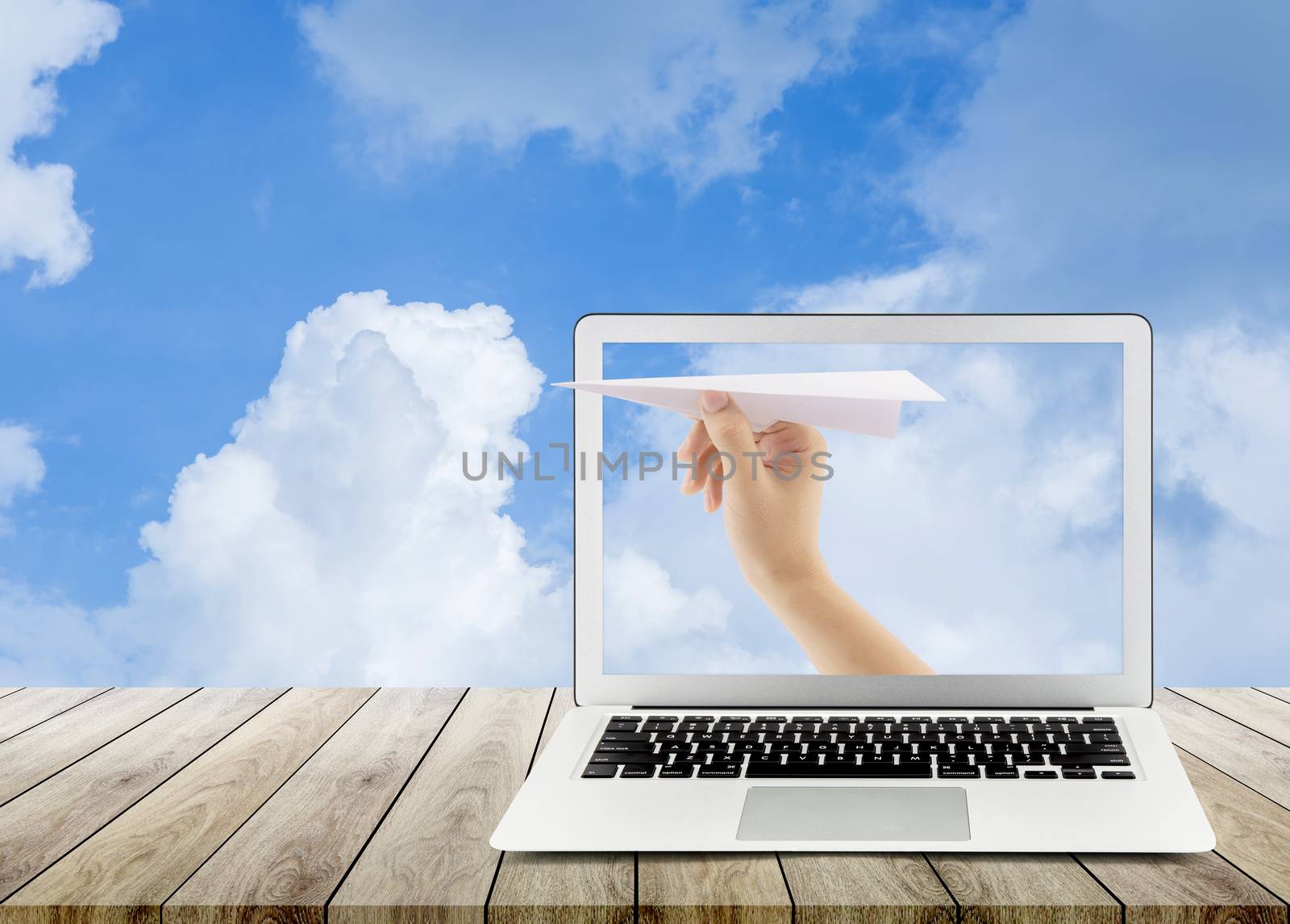 Hand with paper plane with laptop on wood table against blue sky by nnudoo