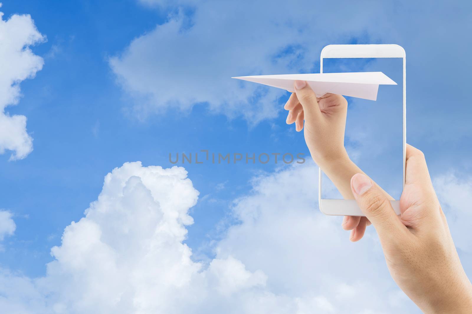 Hand with paper plane with mobile phone against blue sky sending by nnudoo