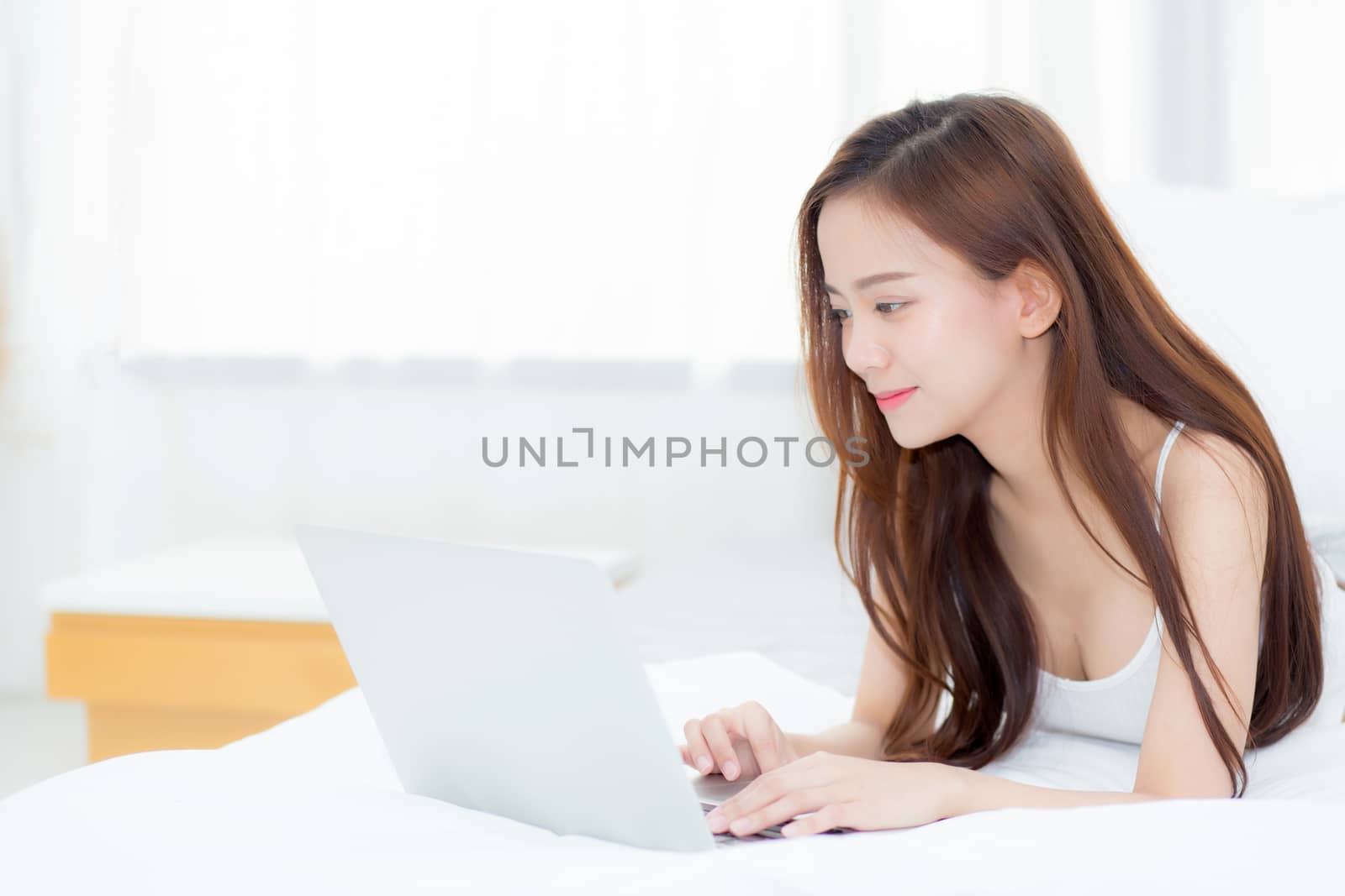 Beautiful asian young woman lying on bed using laptop at bedroom for leisure and relax, freelance with girl working notebook, communication concept.