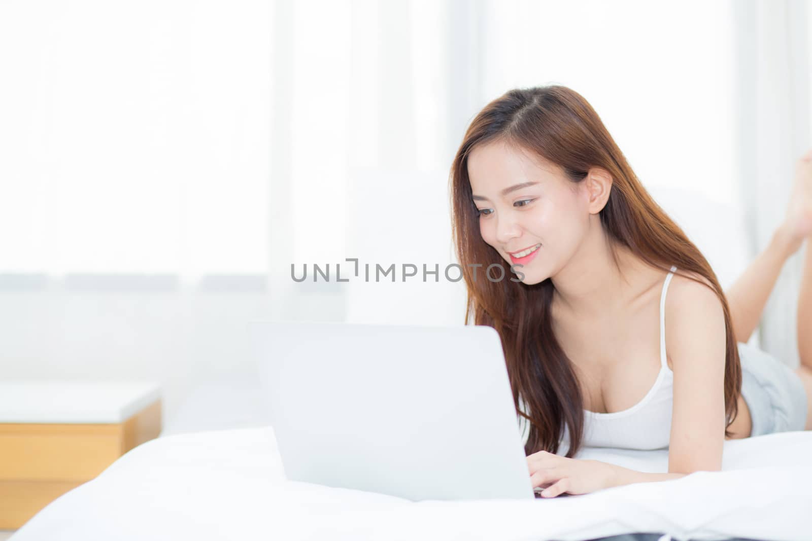 Beautiful asian young woman lying on bed using laptop at bedroom by nnudoo