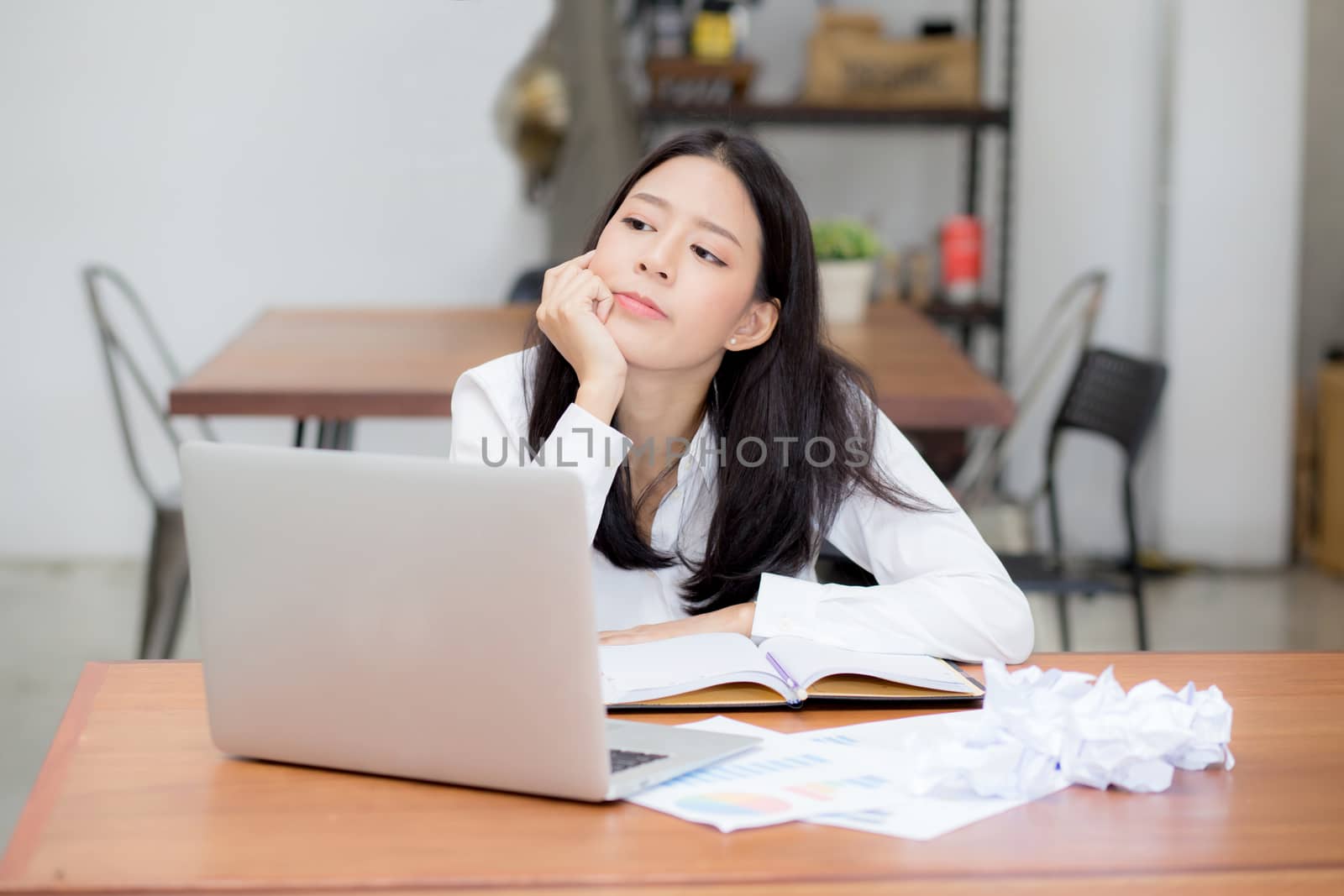 Beautiful asian young woman working online problem with laptop and think project and paper crumpled on table with idea at modern cafe shop, business and freelance concept.