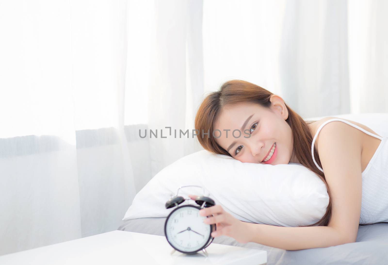 Beautiful asian young woman turn off alarm clock in morning, wake up for sleep with alarm clock, relax and lifestyle concept.