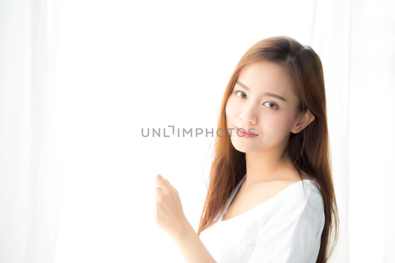 Beautiful young asian woman standing the window and smile while wake up with sunrise at morning, lifestyle and relax concept.
