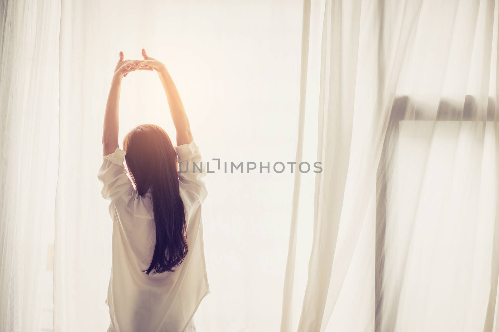 Beautiful young asian woman stretch and relax in bed after wake up morning at bedroom, back view, new day and resting for wellness, lifestyle concept.