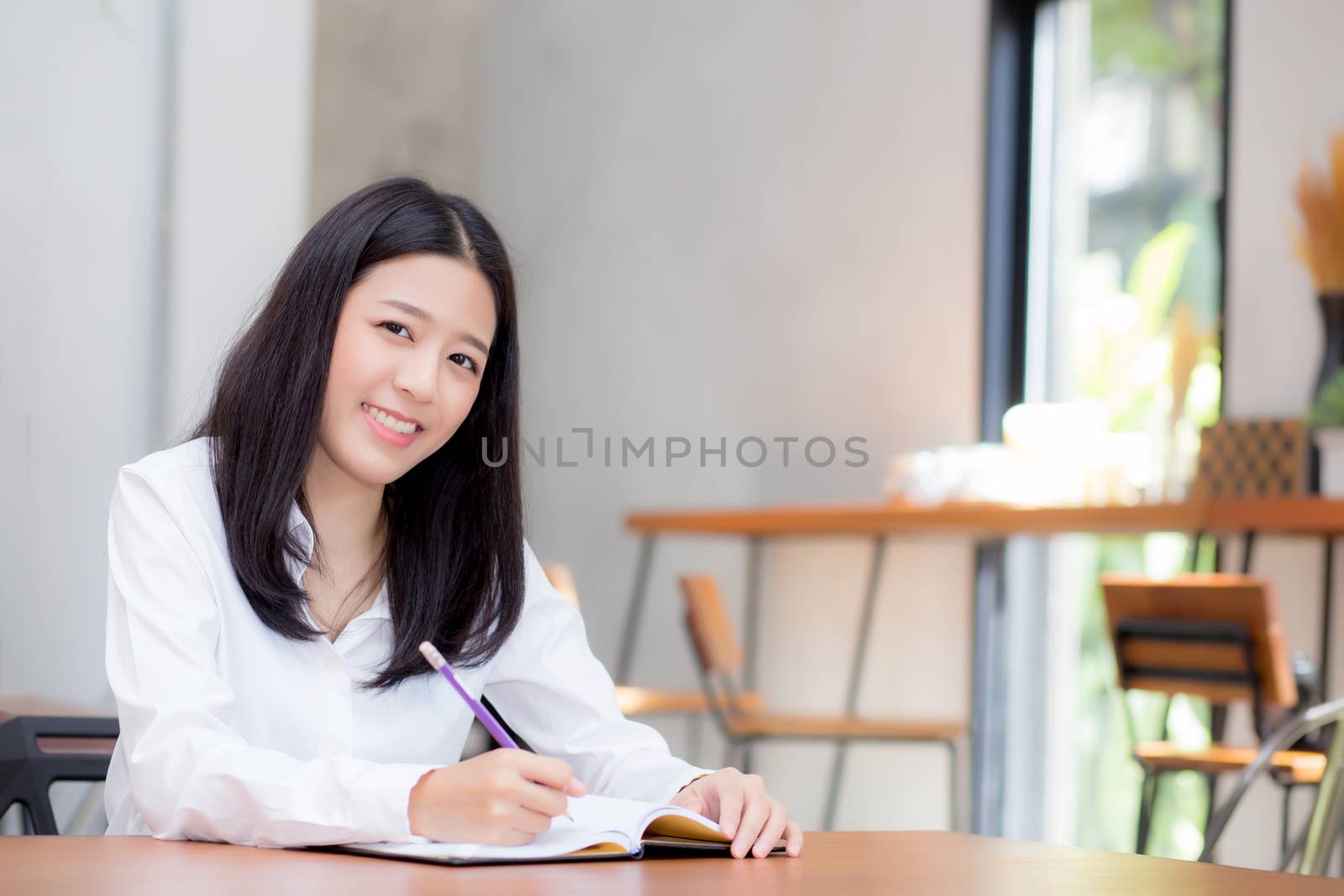 Beautiful business asian young woman writing on notebook on table, girl work at coffee shop, freelance business concept.