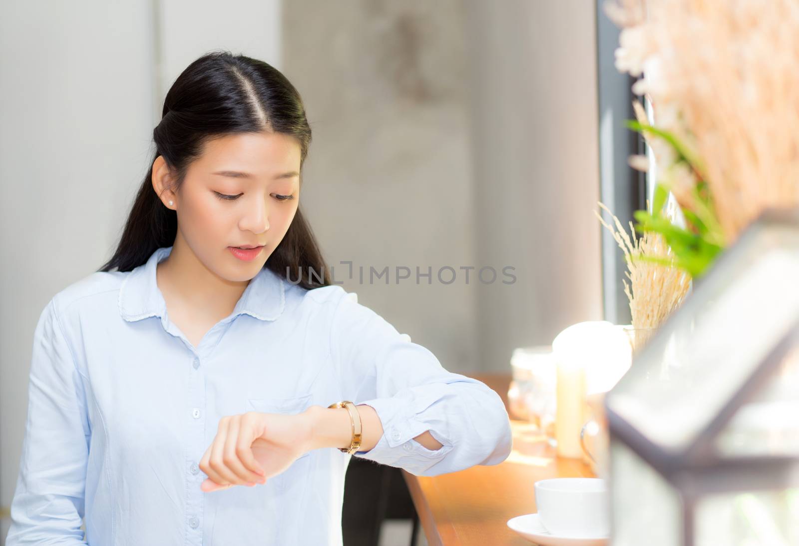 Beautiful asian young woman look at watch waiting for friend or someone, girl checking clock with appointment at coffee shop.
