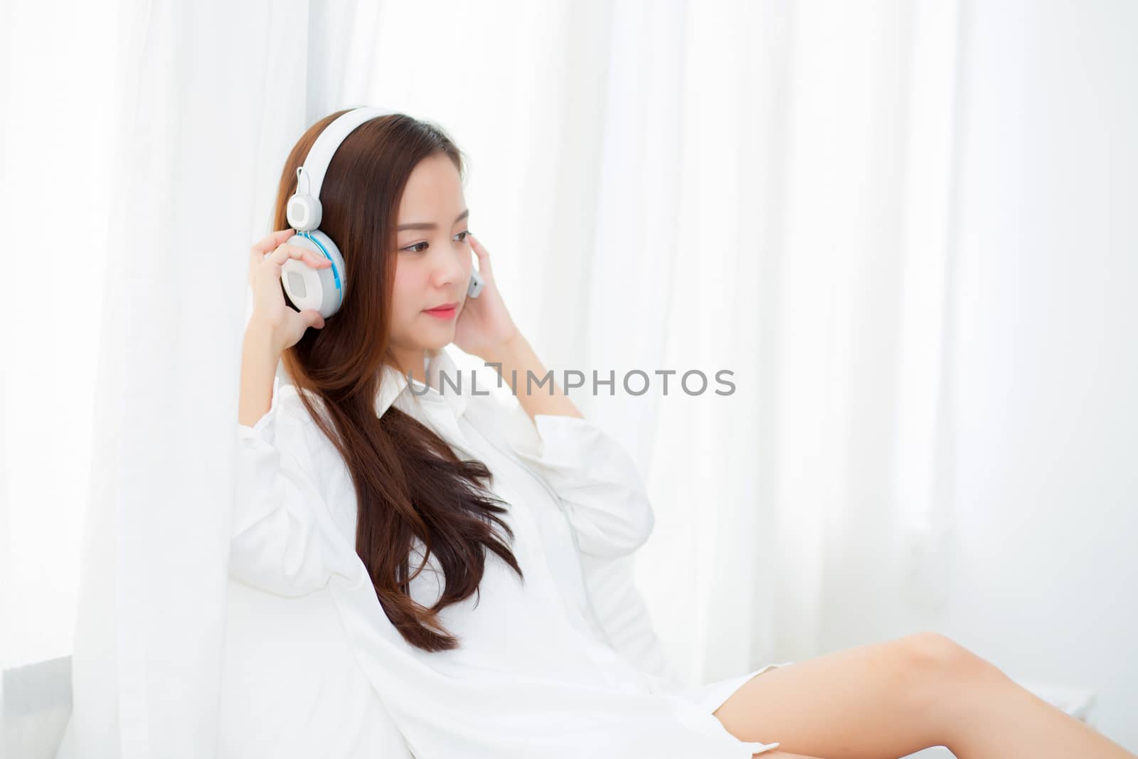 Beautiful asian young woman enjoy listen music with headphone while sitting in bedroom, relax girl with earphone internet online, leisure and technology concept.