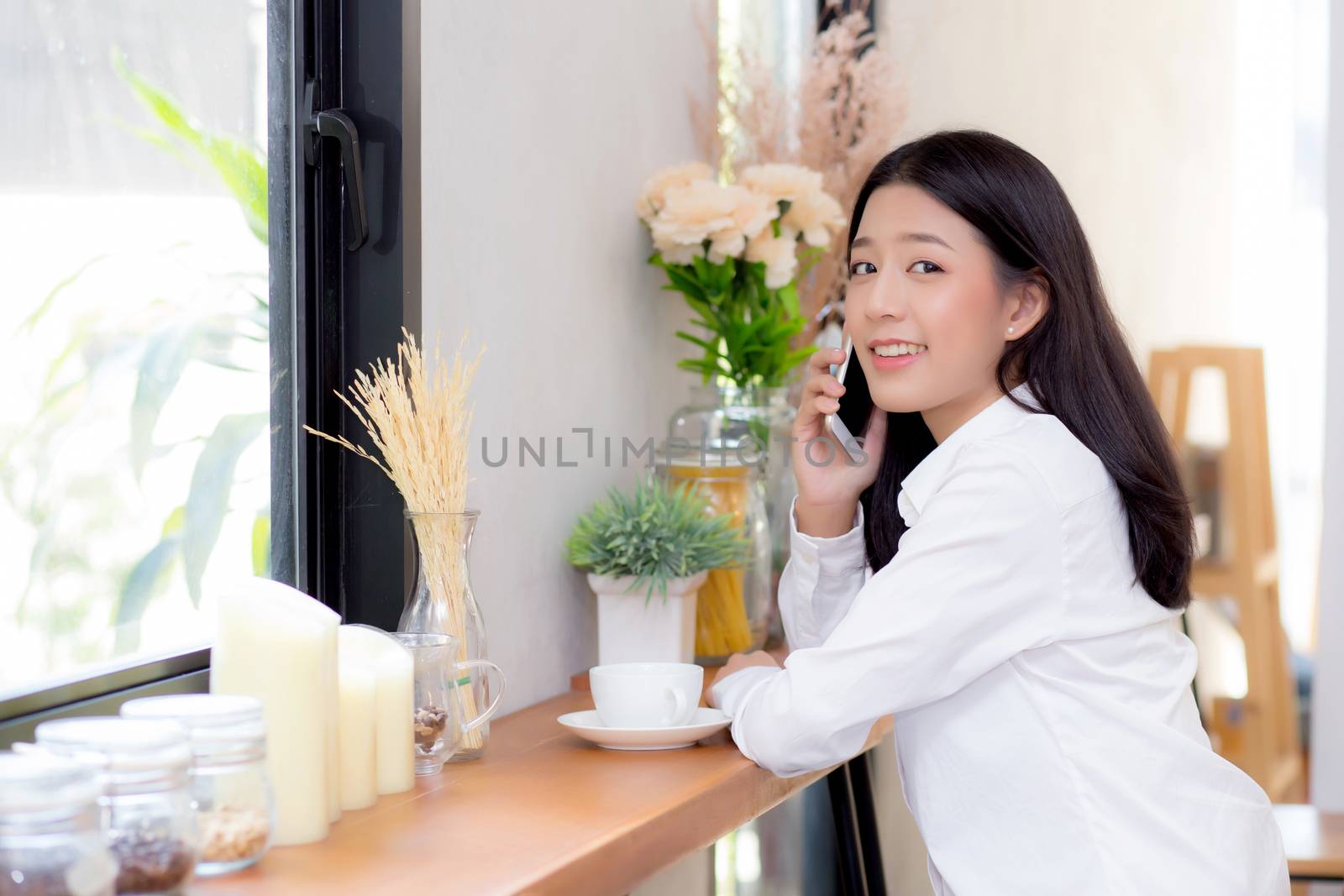 Beautiful young asian woman talking phone and smile in the coffee shop, businesswoman sitting in cafe free time, freelancer female calling telephone, communication concept.