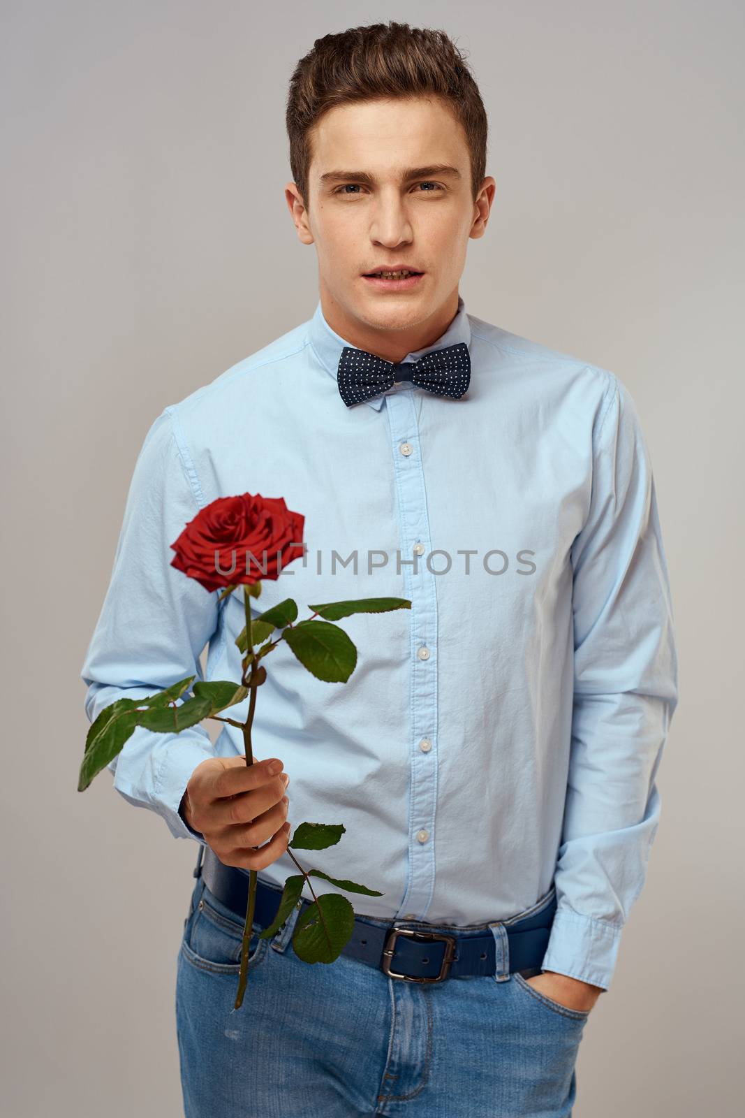 Romantic man with a red rose and in a blue shirt with a bow tie around his neck gray background. High quality photo